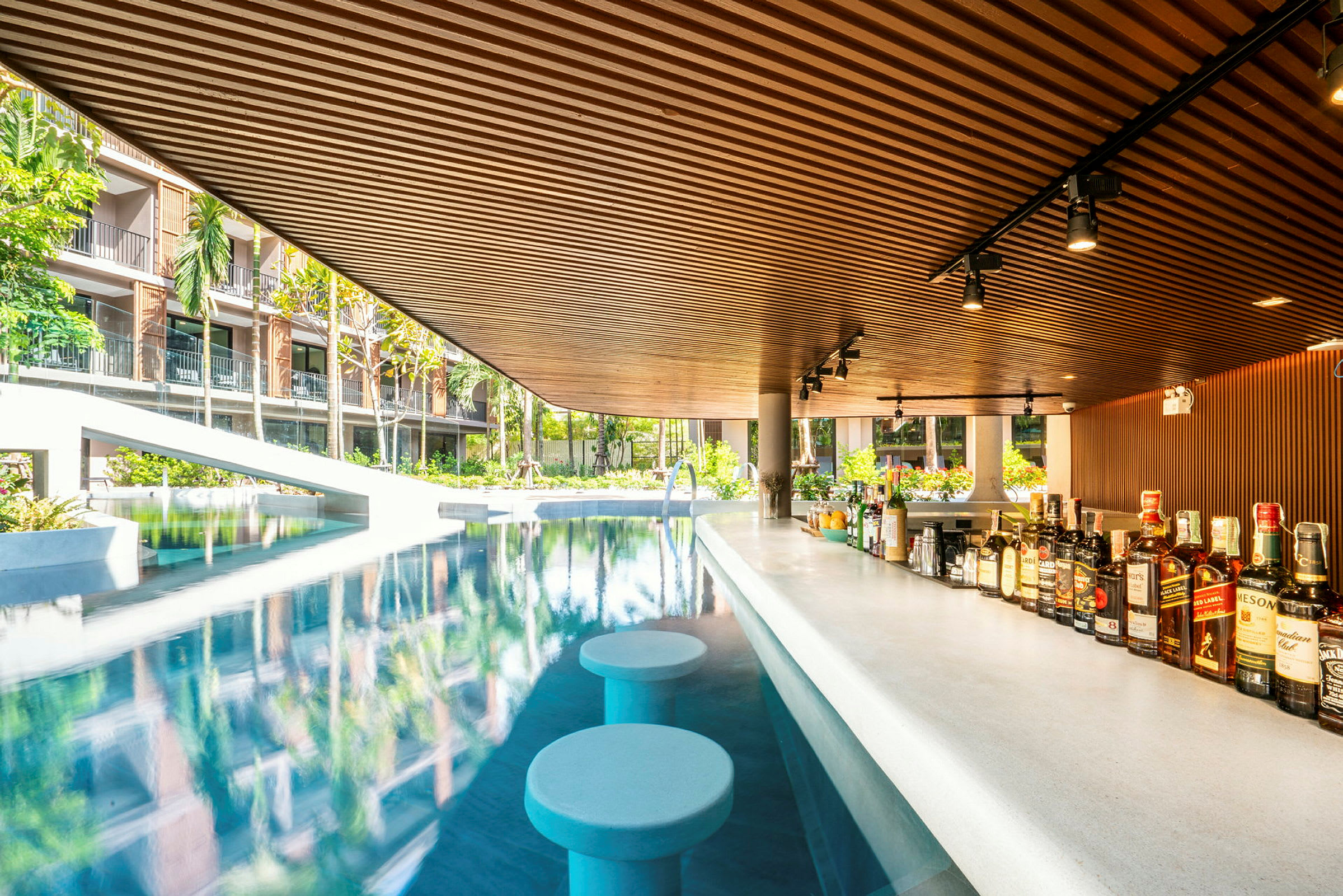 En poolbar med siddepladser i vandet, omgivet af grønne områder og hotelbygninger. (AI-genereret tekst)
