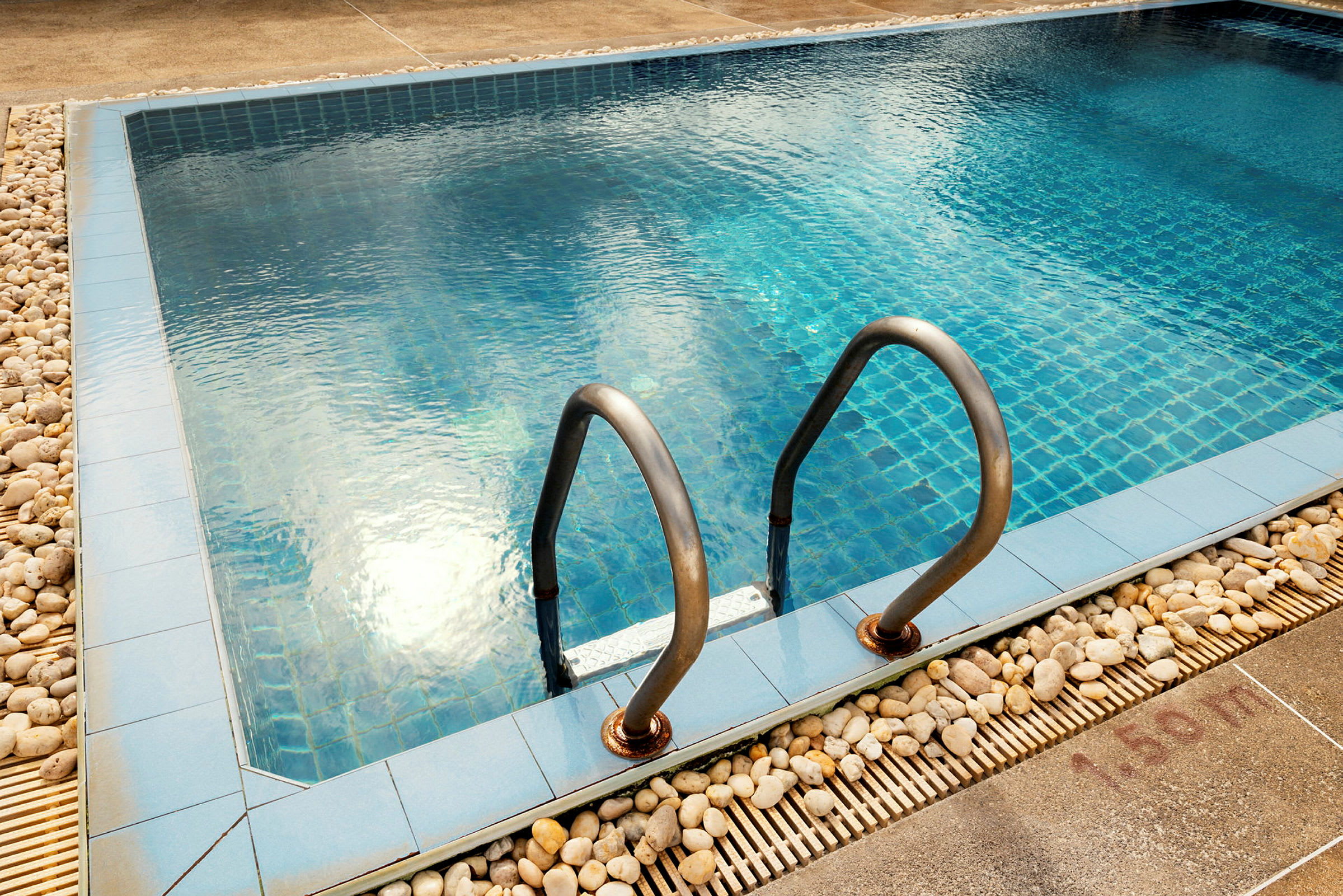 En pool med blå keramisk bund og stålgreb ved kanten. (AI-genereret tekst)