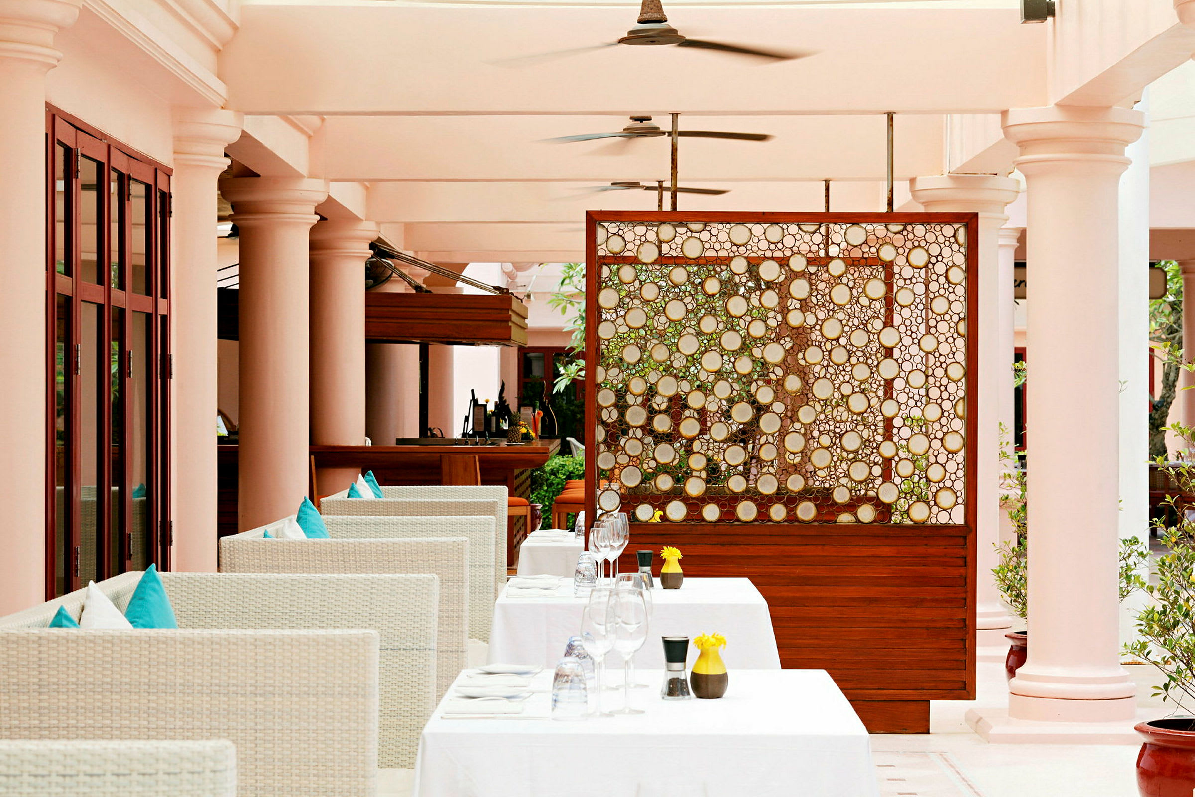 Restaurant med hvide møbler, grønne puder og borde med gule dekorationer under en balkon. (AI-genereret tekst)