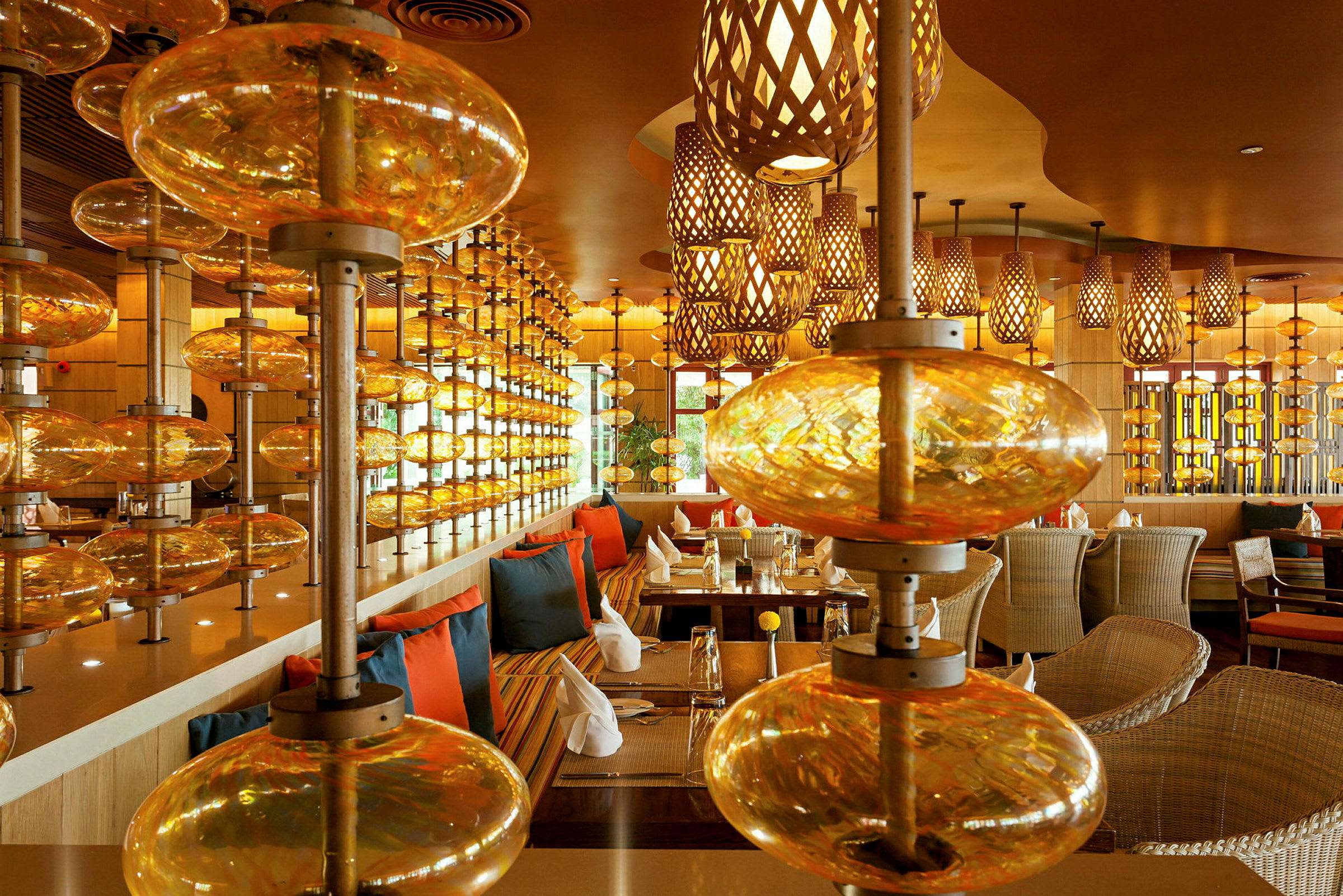 Interiør af en restaurant med varm belysning, borde med servietter og stole samt dekorationsglas installeret som rumdelere. (AI-genereret tekst)