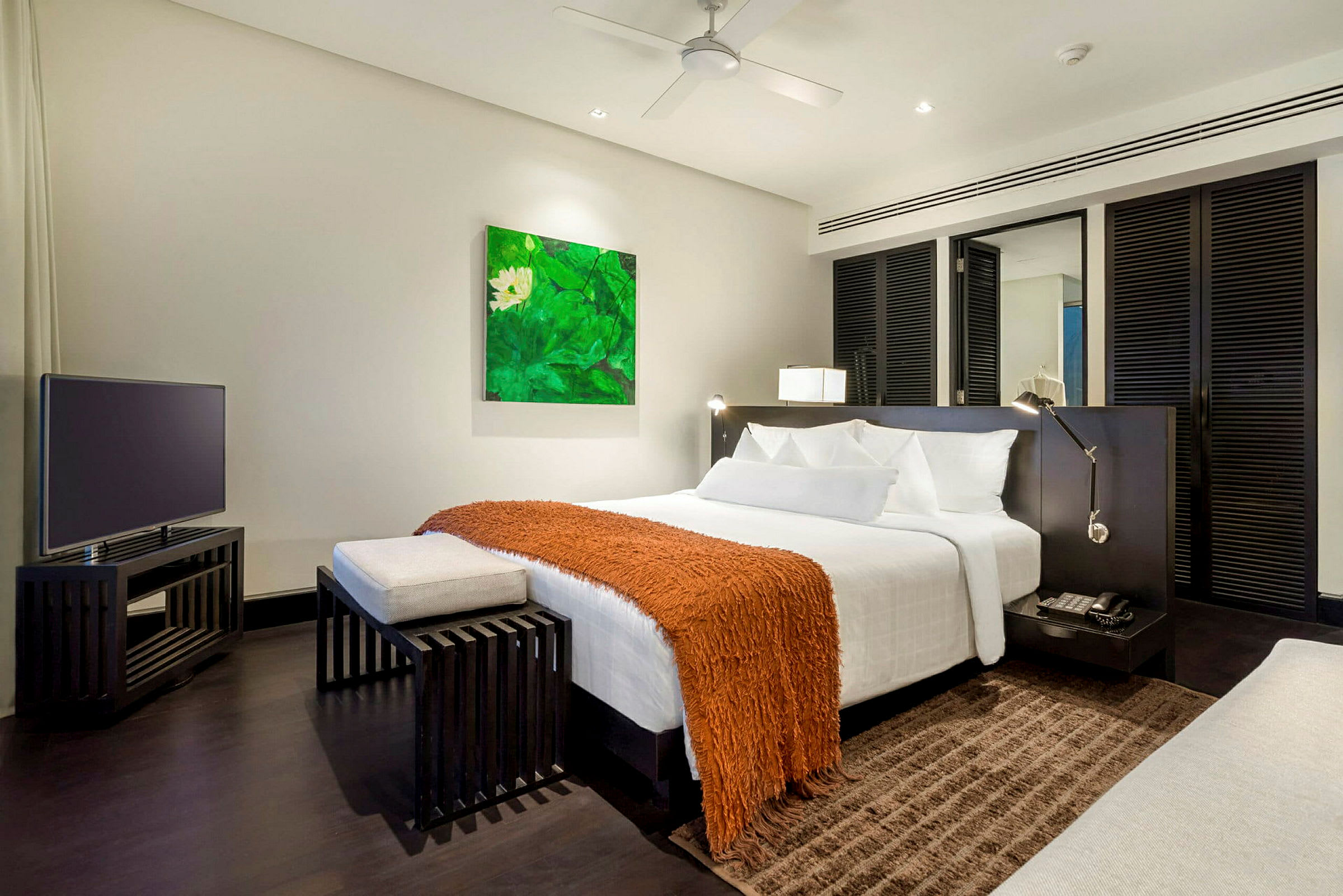 Et moderne hotelværelse med en dobbeltseng, et orange tæppe og et fjernsyn på et sort bord. (AI-genereret tekst)