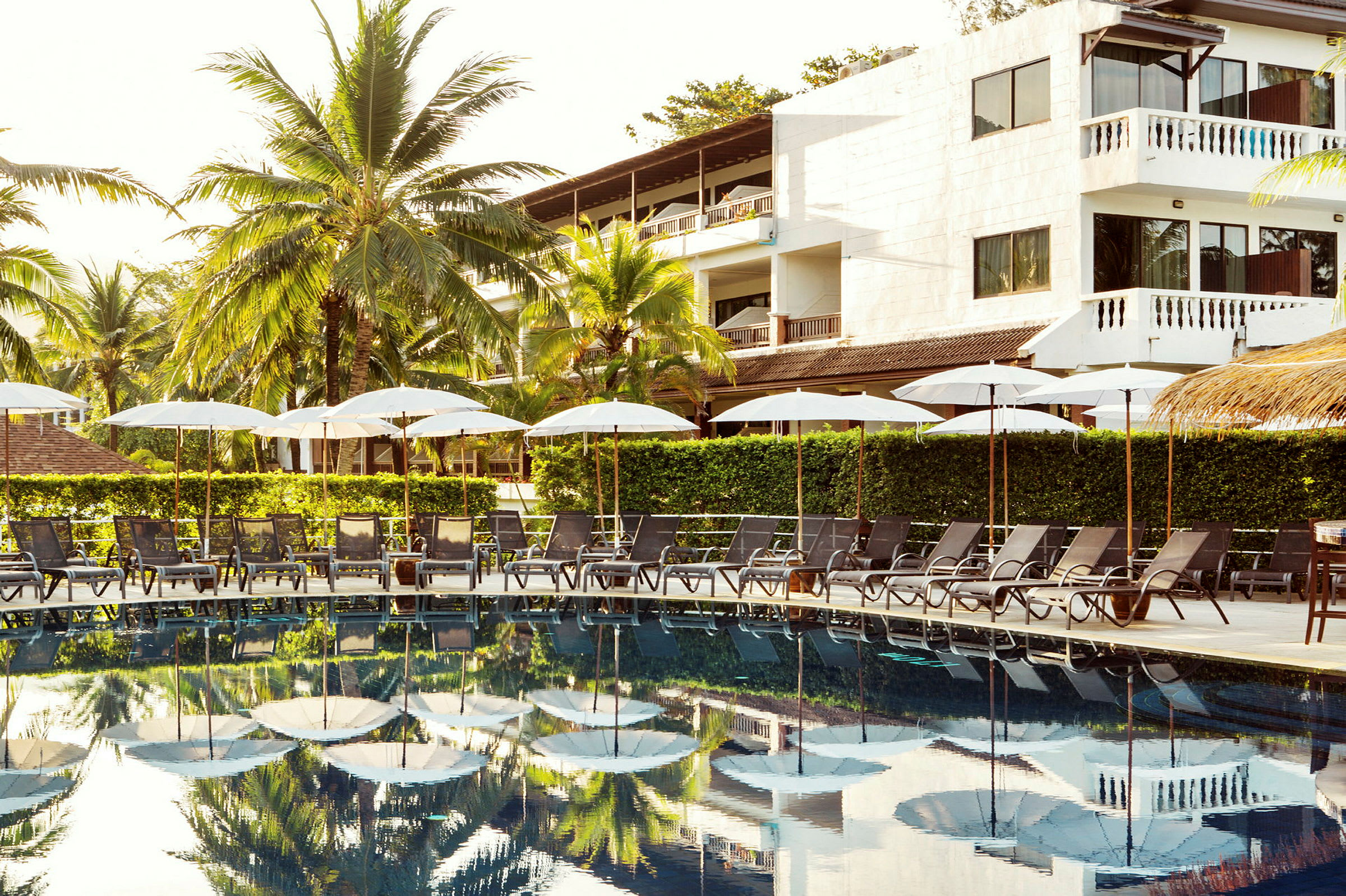 Udendørsmøbler med parasoller ved en pool i en tropisk omgivelser. (AI-genereret tekst)