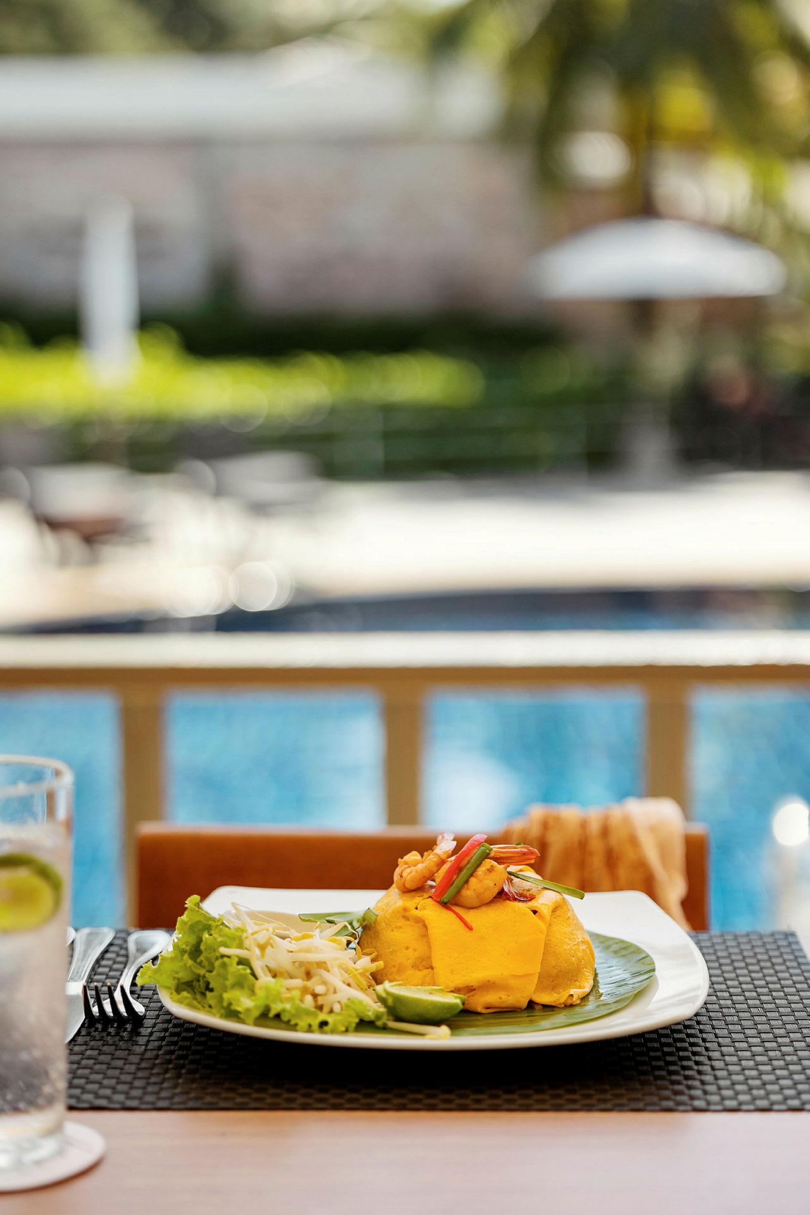 En tallerken med mad, inklusive en omelet og grøntsager, på et bord ved en pool. (AI-genereret tekst)