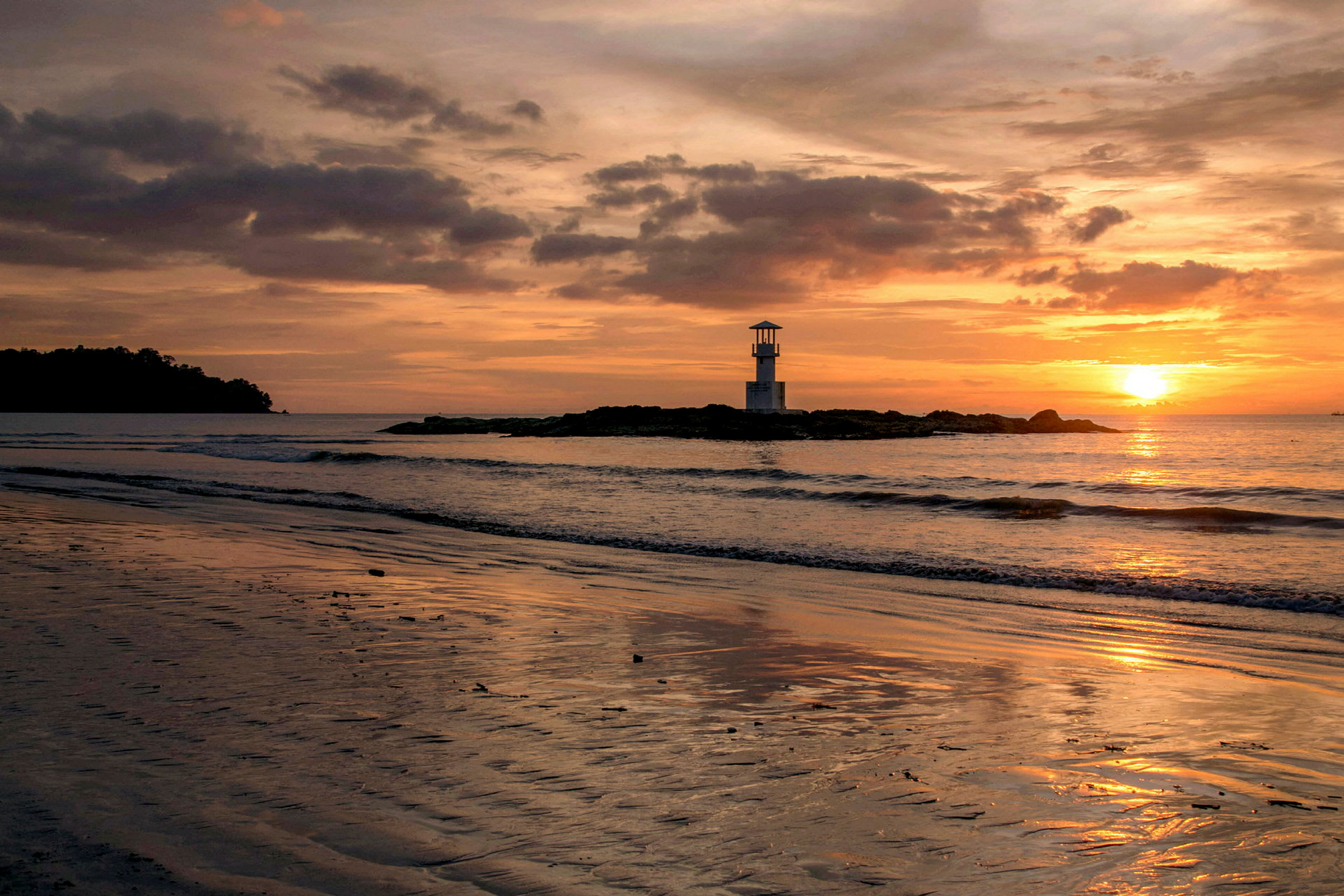 Solnedgang ved en strand, med et fyrtårn på et klippefremspring og himlen farvet i orange og rosa nuancer. (AI-genereret tekst)