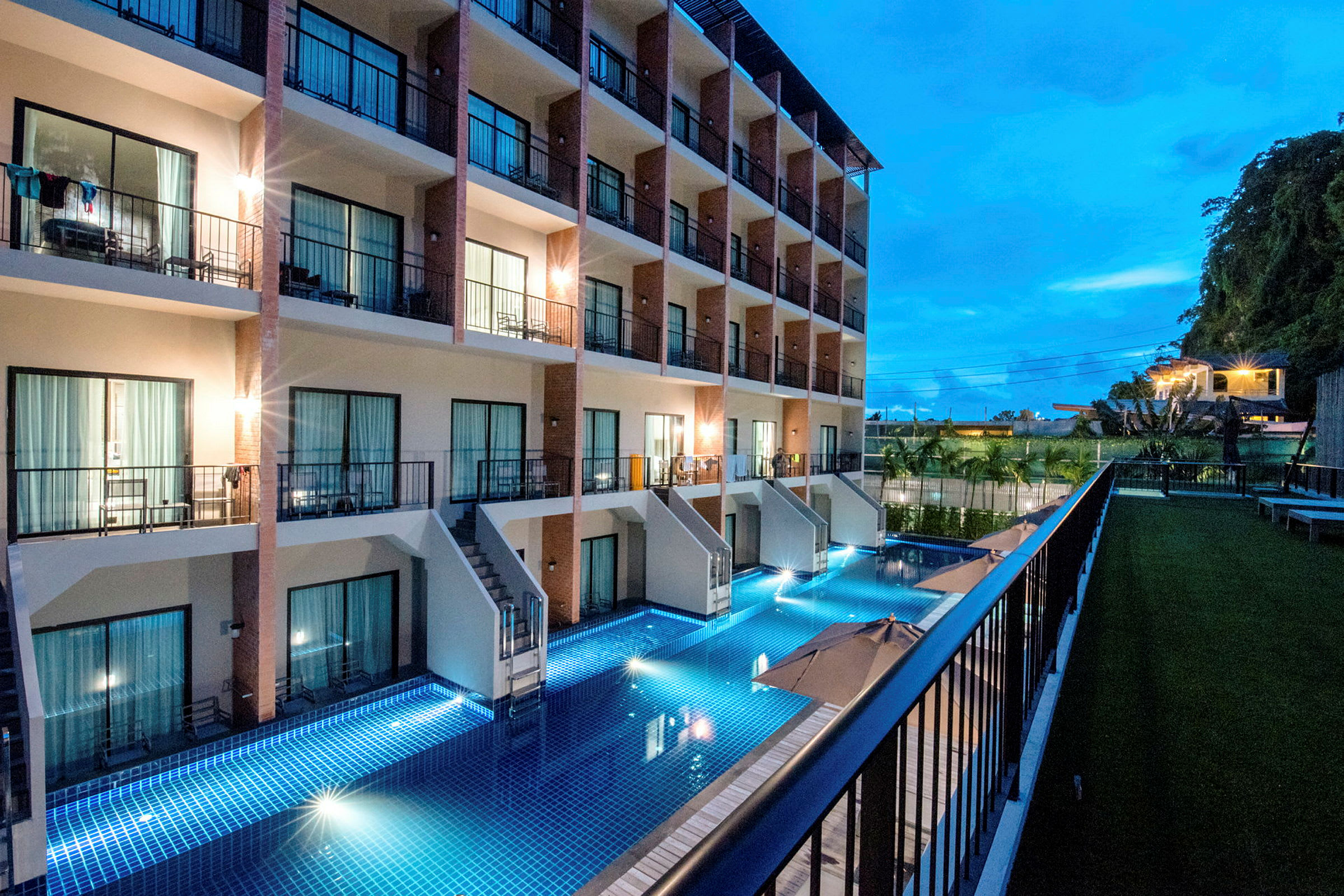 Et hotel om aftenen med en pool ved facaden og altaner tilhørende værelserne. (AI-genereret tekst)