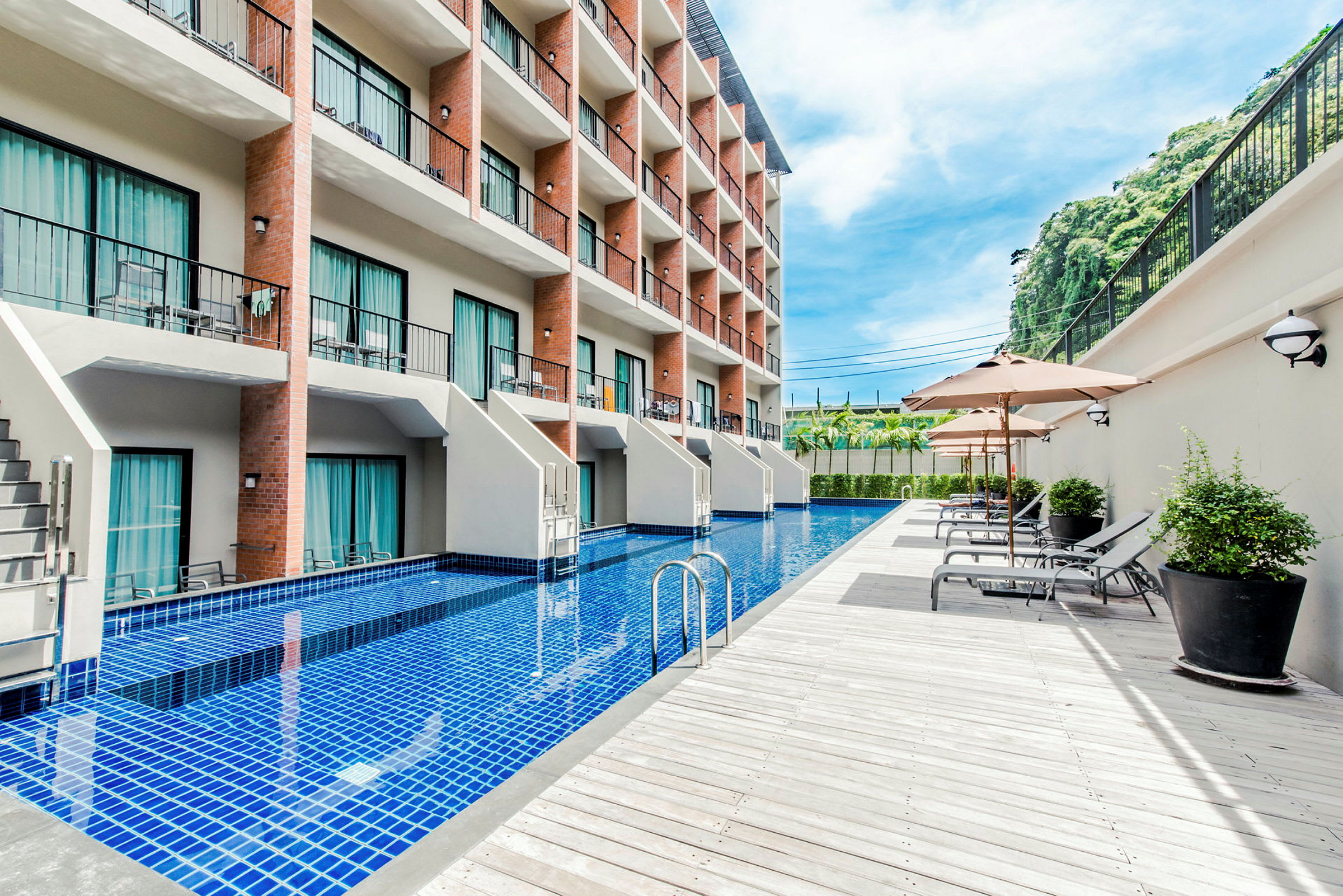 Et hotel med flere etager og en lang pool foran bygningen, omgivet af liggestole og parasoller. (AI-genereret tekst)