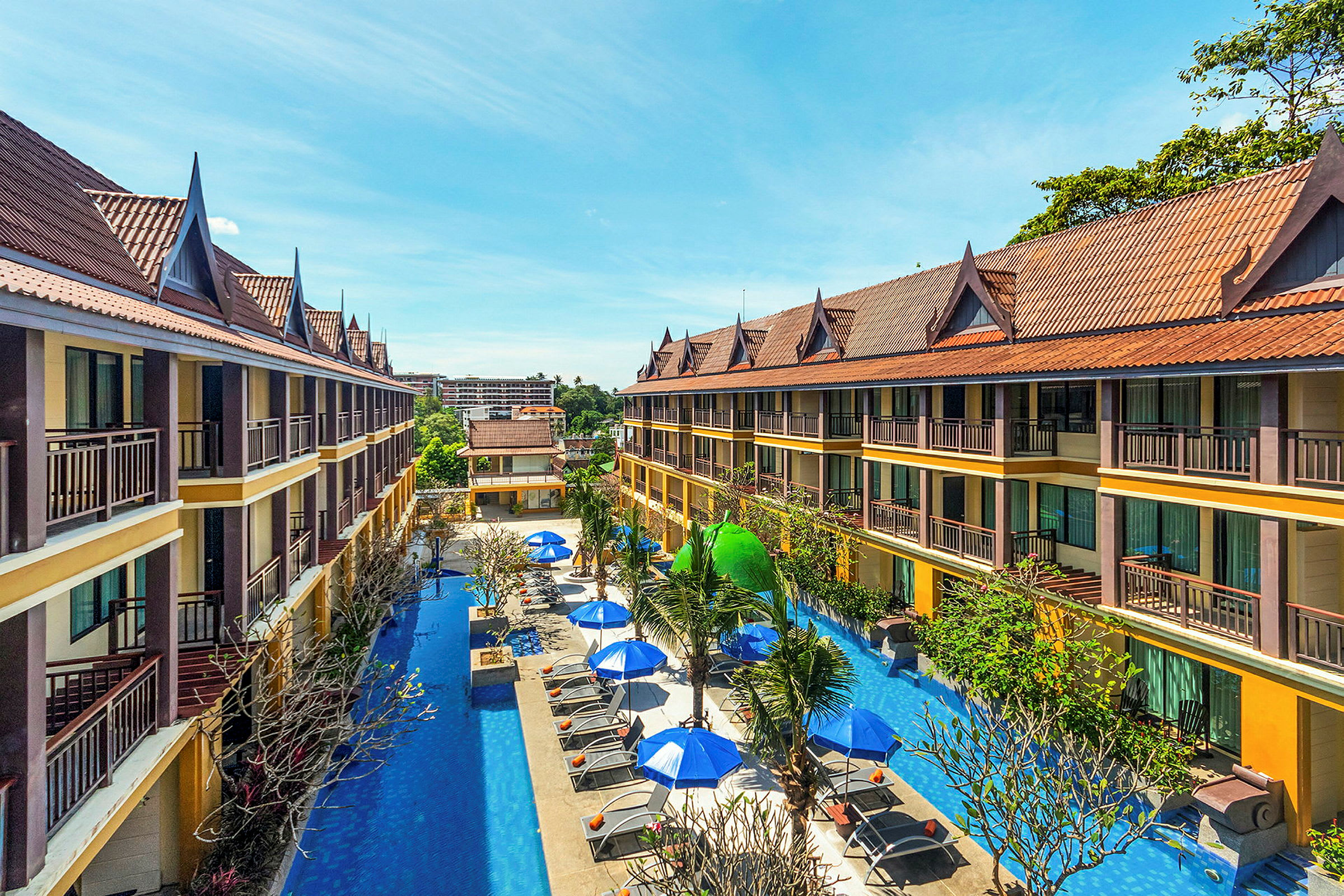 Toetagers hotelbygninger med skrånende tage omgiver en pool med liggestole og parasoller. (AI-genereret tekst)