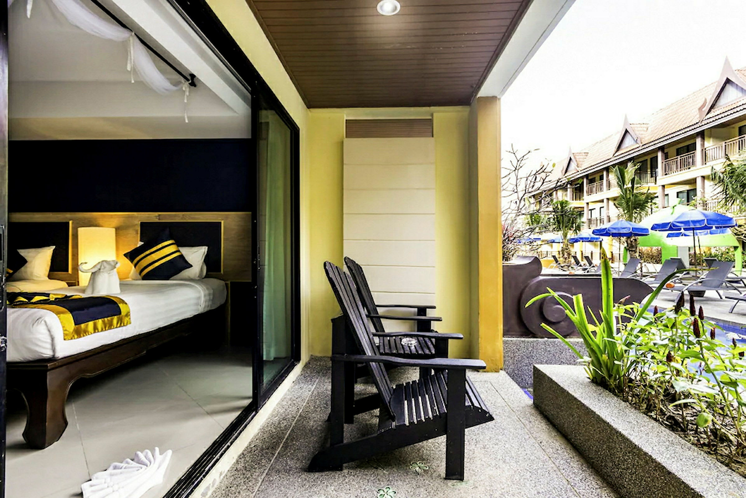 Billede af en hotelleterrasse med to træstole vendt mod en pool med parasoller og solsenge. Hotelværelset ses gennem en skydedør. (AI-genereret tekst)