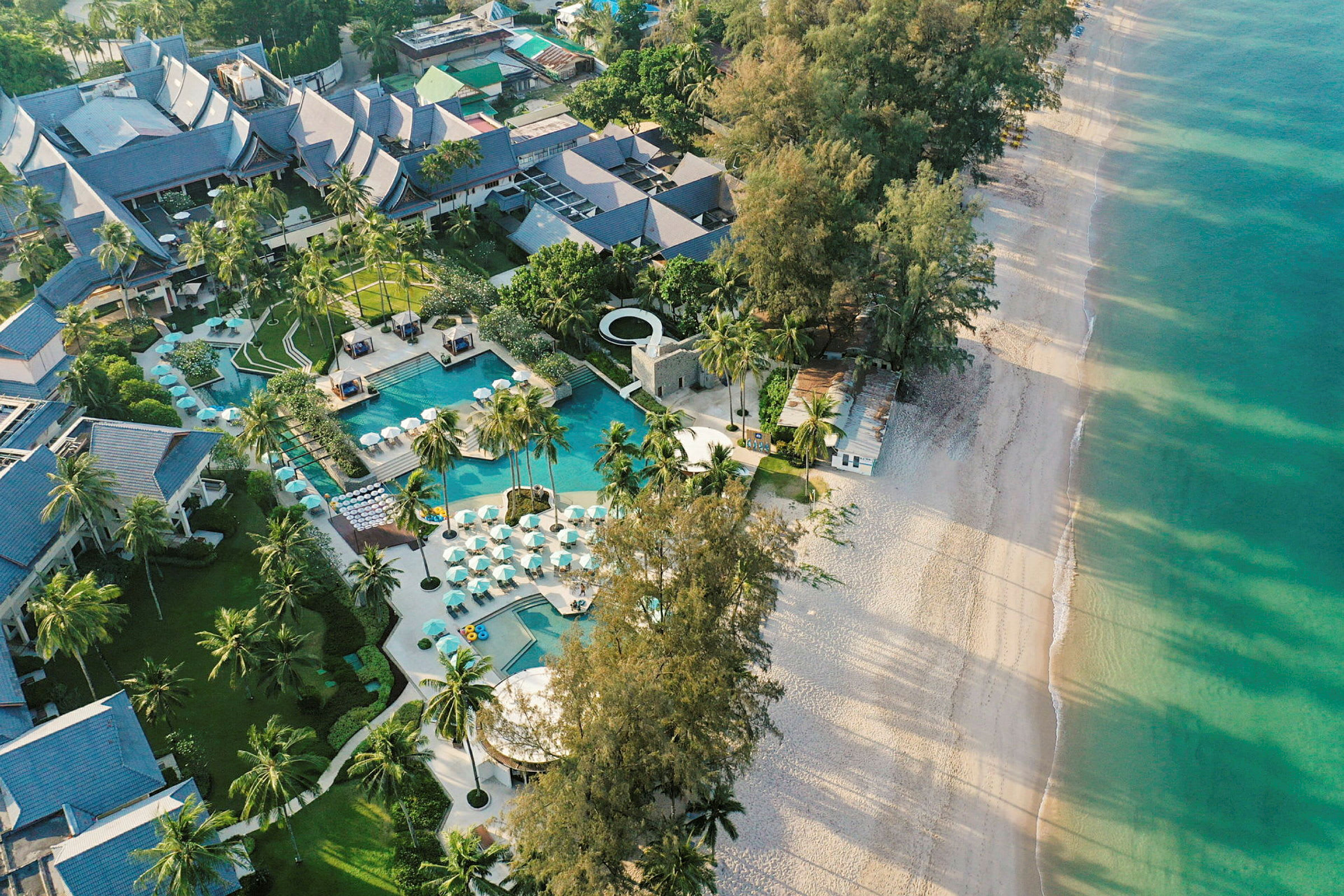 Luftfoto af et resort med pool og omgivet af palmer ved en sandstrand. (AI-genereret tekst)