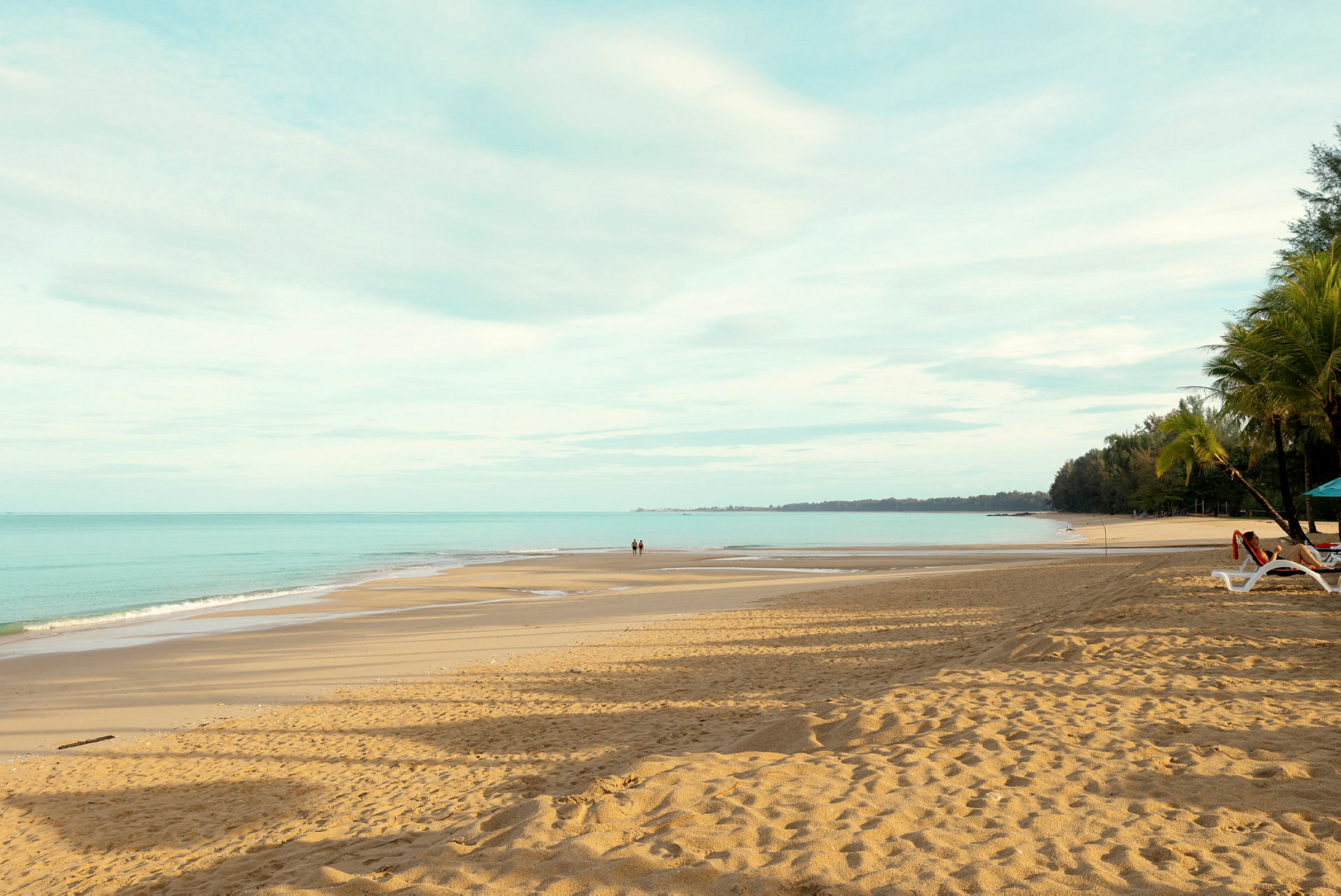 En sandstrand med udsigt over havet, to personer går på stranden. (AI-genereret tekst)