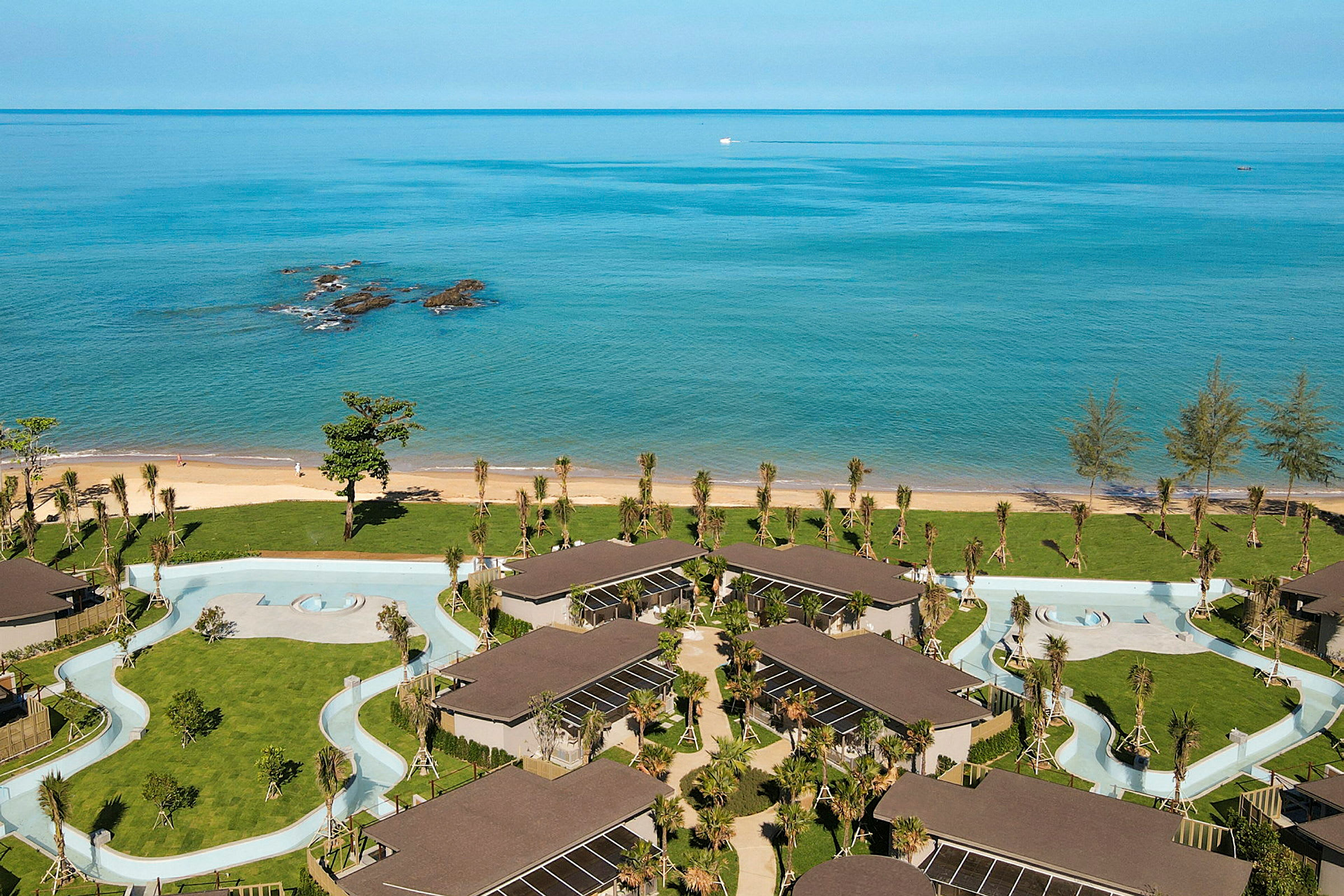 Luftfoto af et strandhotel med bygninger, græsplæner og en snoet pool. (AI-genereret tekst)