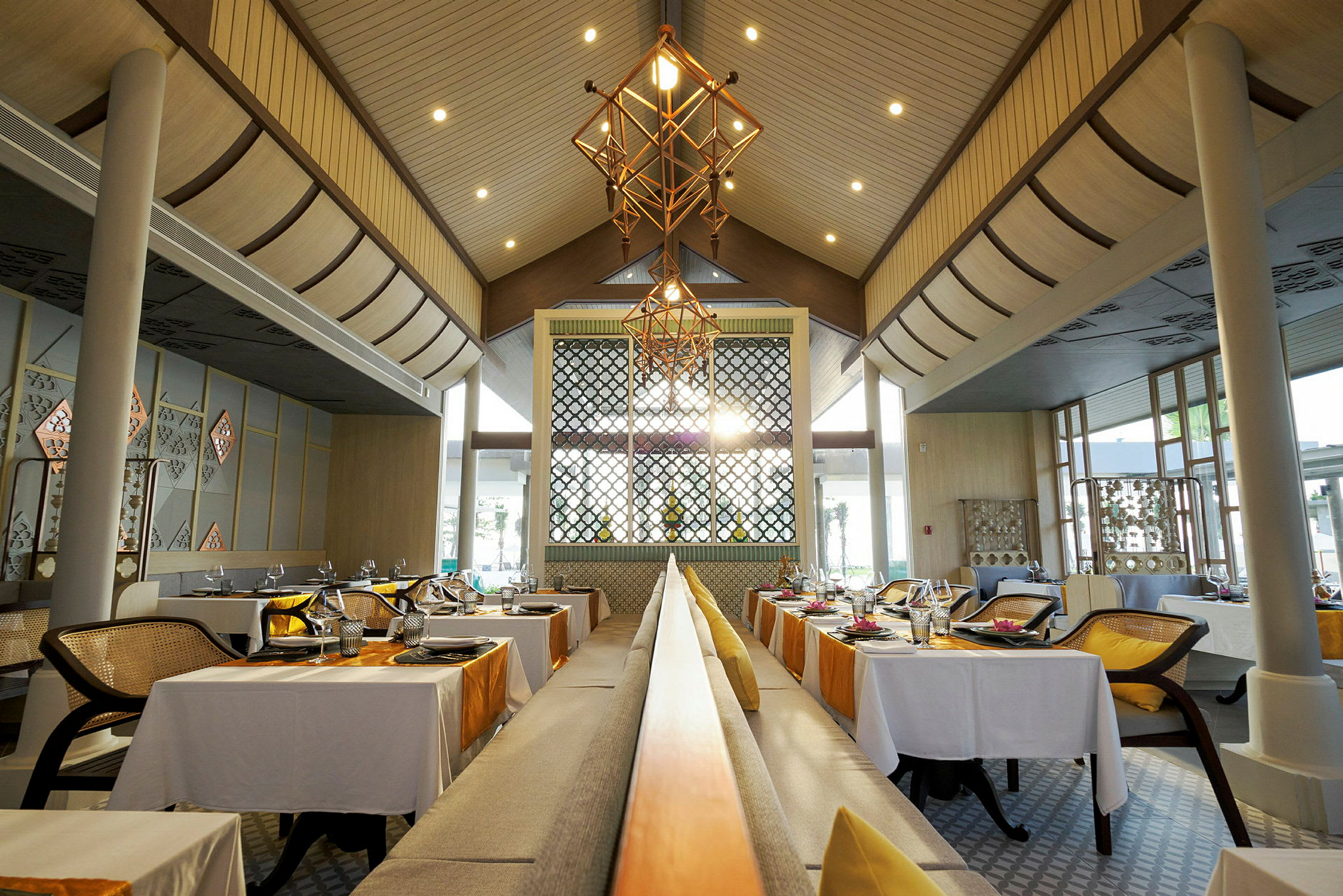 Billede af en elegant restaurant med borde dækket til middag, dekoreret med hvide duge og orange løbere samt moderne loftsbelysning. (AI-genereret tekst)