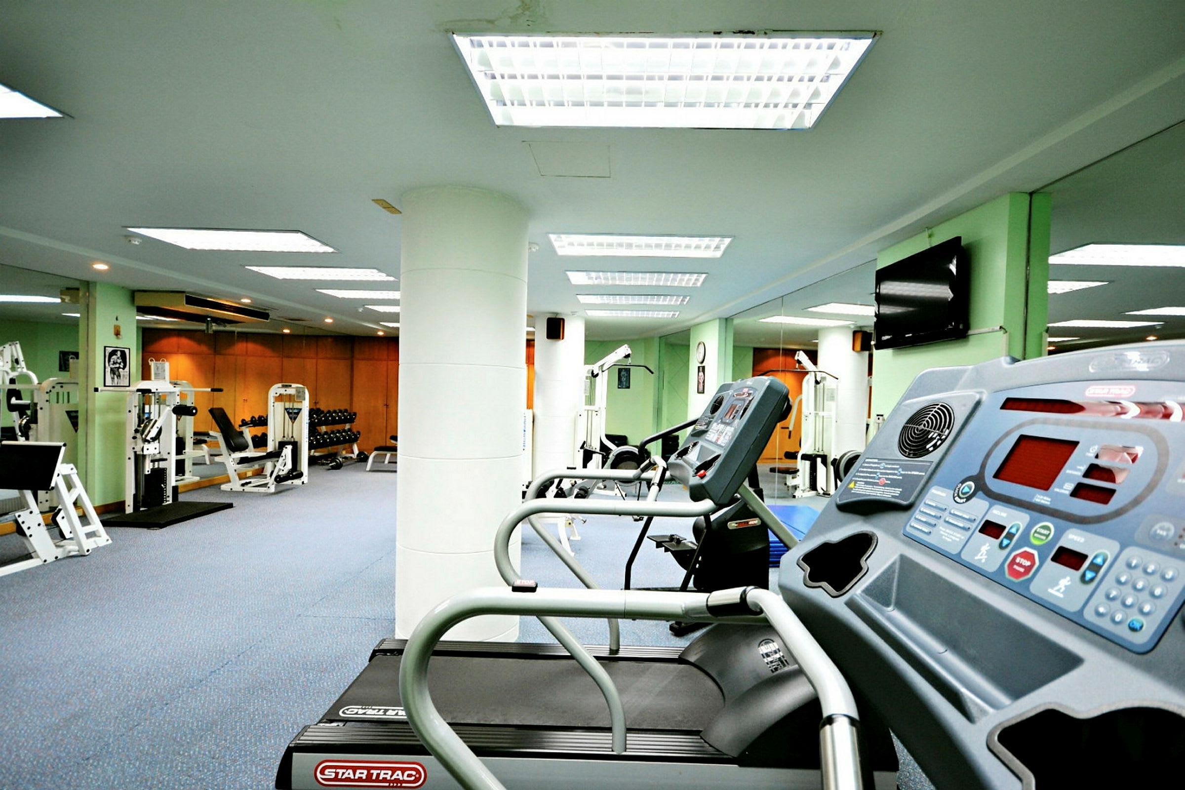 Et fitnesscenter med træningsmaskiner, herunder løbebånd, styrketræningsudstyr og vægte. (AI-genereret tekst)