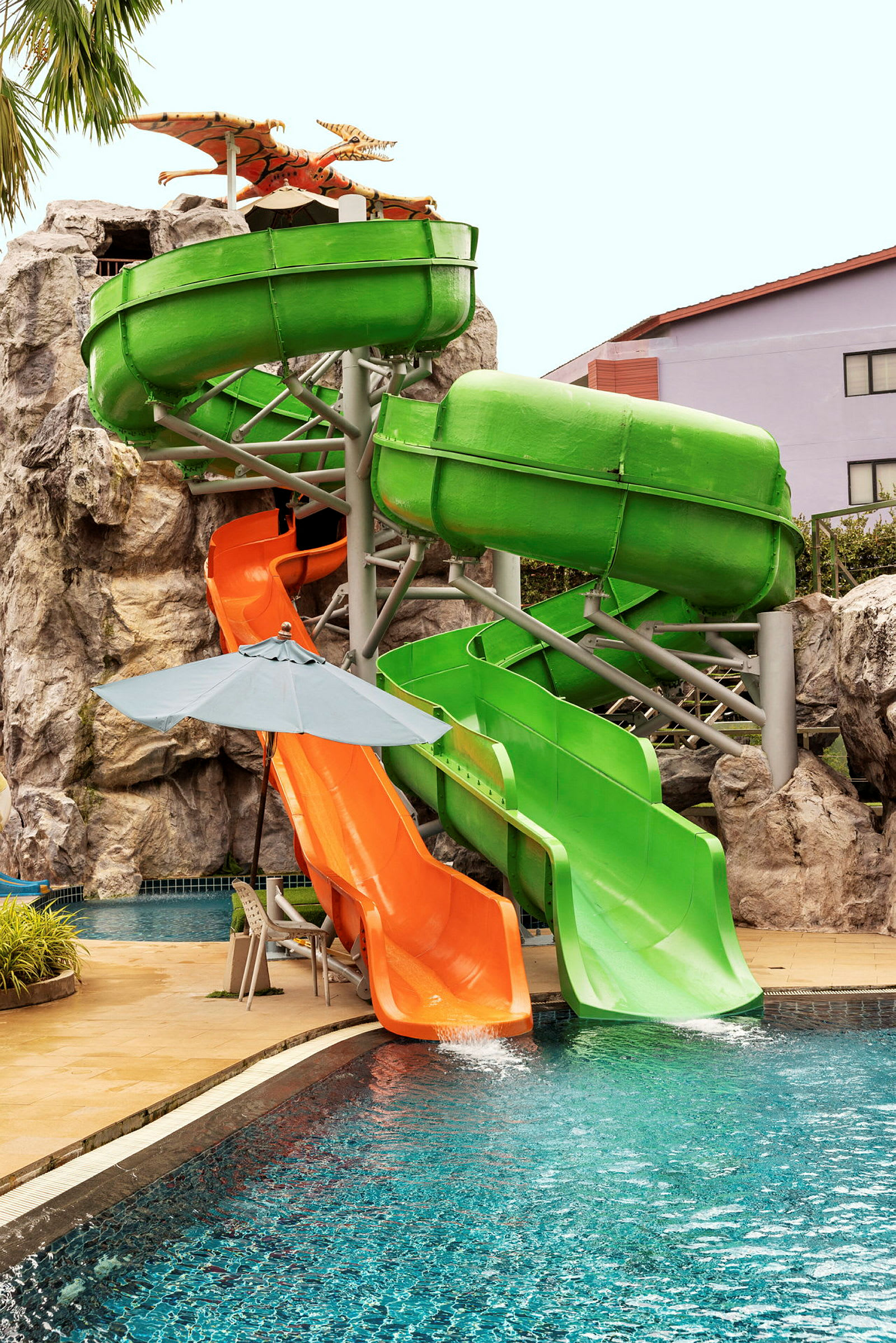 To vandrutsjebaner, en grøn og en orange, der fører ned i en swimmingpool. (AI-genereret tekst)