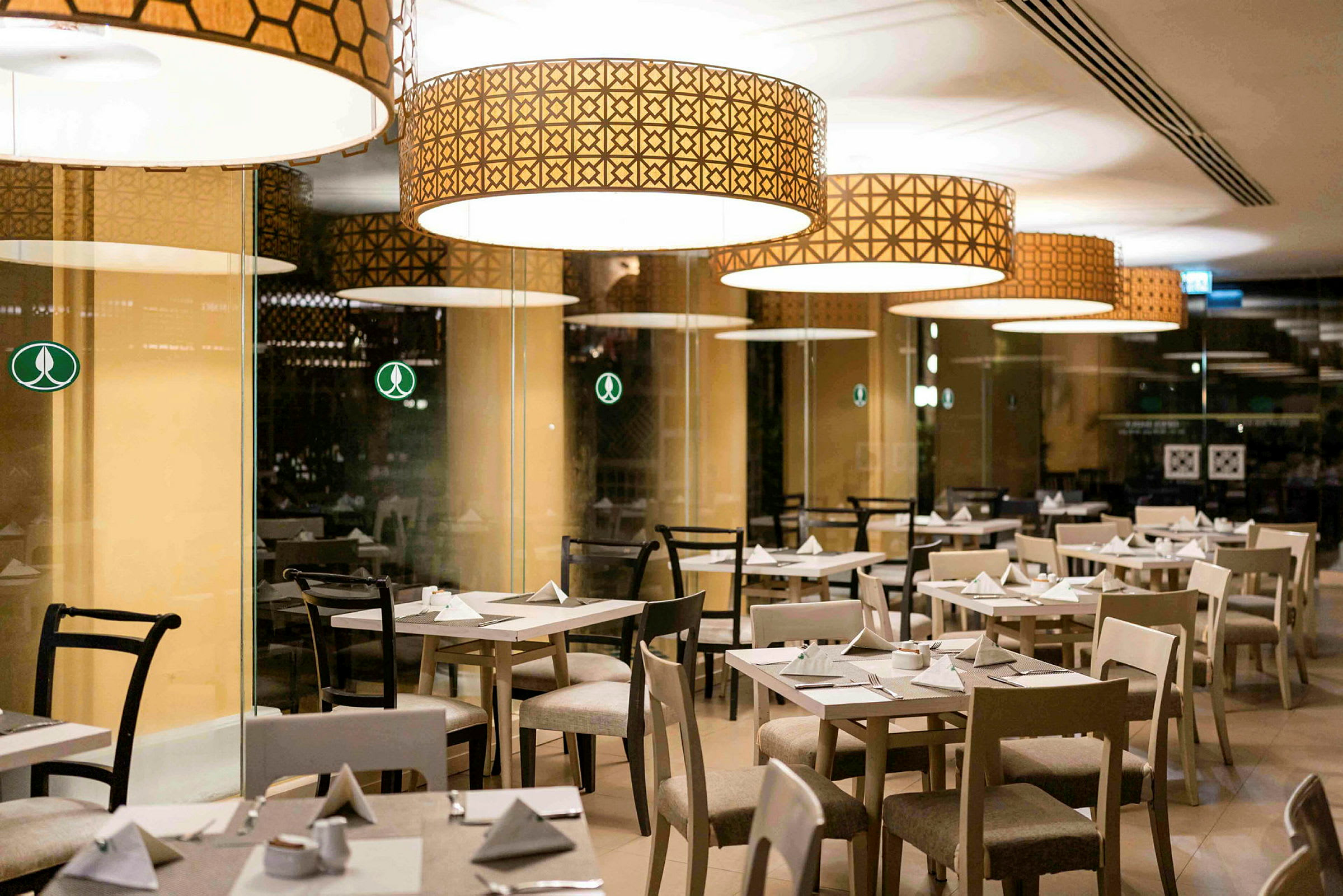 Billede af en restaurant med flere dækkede borde og stole under store dekorative lamper. (AI-genereret tekst)