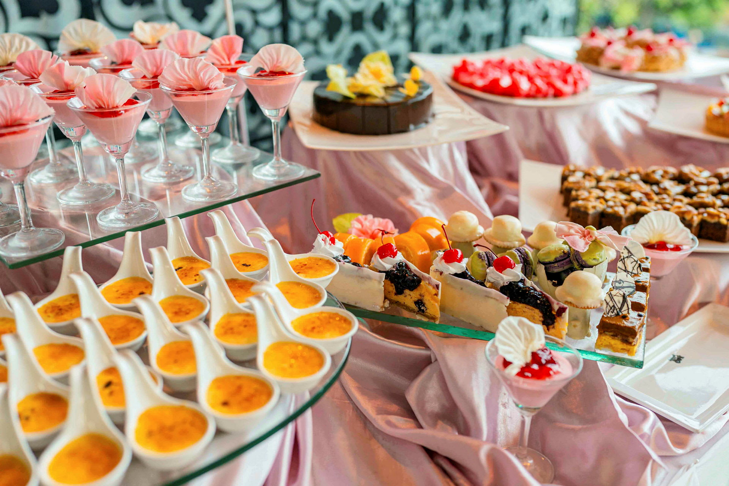 En buffet med forskellige desserter, herunder glas med pink mousse, crème brûlée og dekorerede kager. (AI-genereret tekst)
