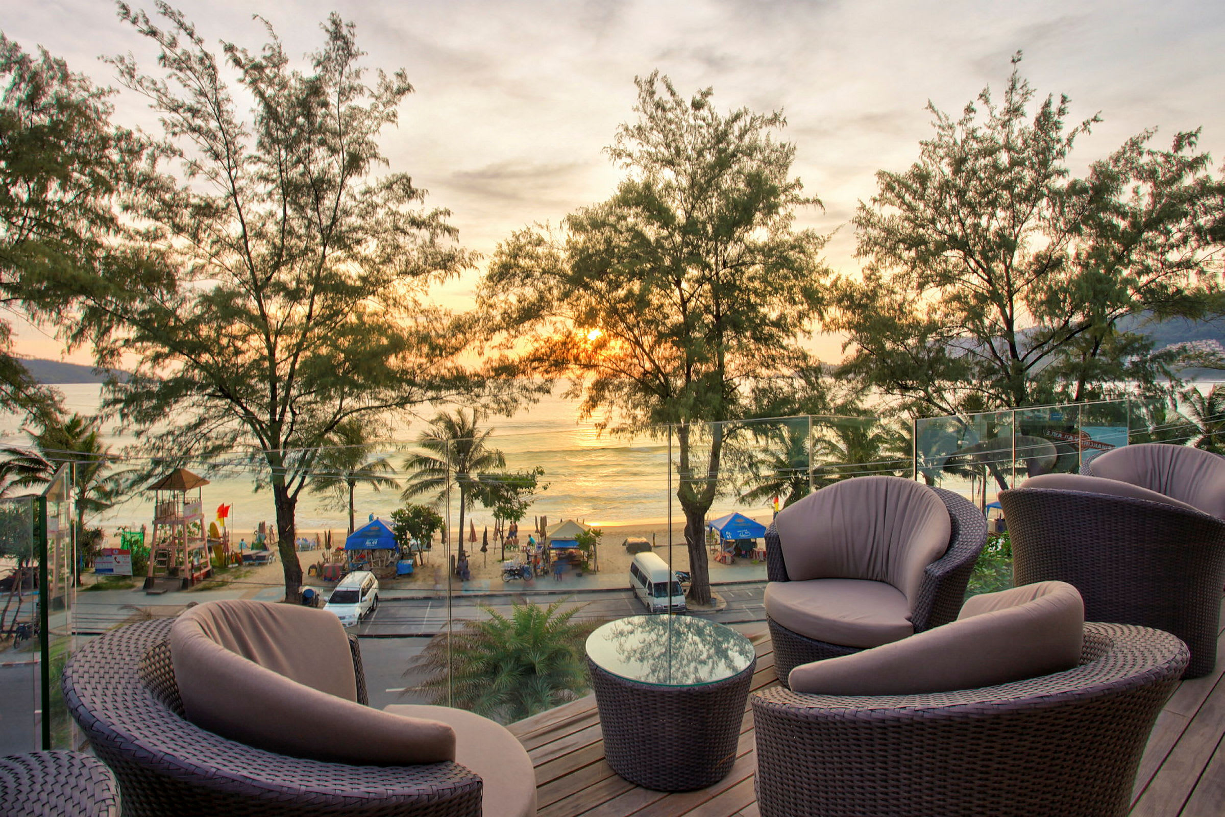 Udendørsmøbler på en terrasse med udsigt over en strand med hav og solnedgang i baggrunden. (AI-genereret tekst)
