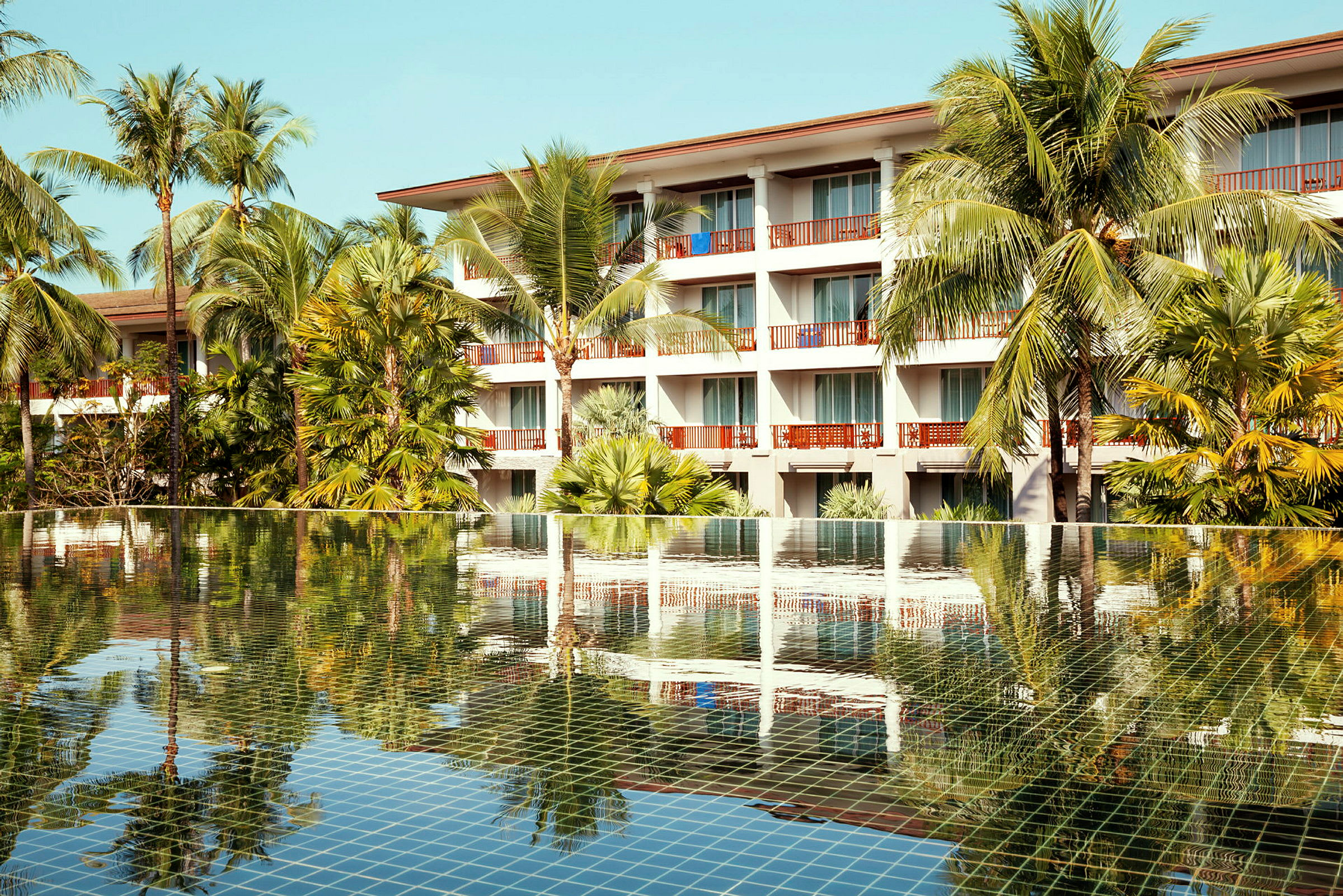 Hotelbygning bag en pool med palmer. (AI-genereret tekst)