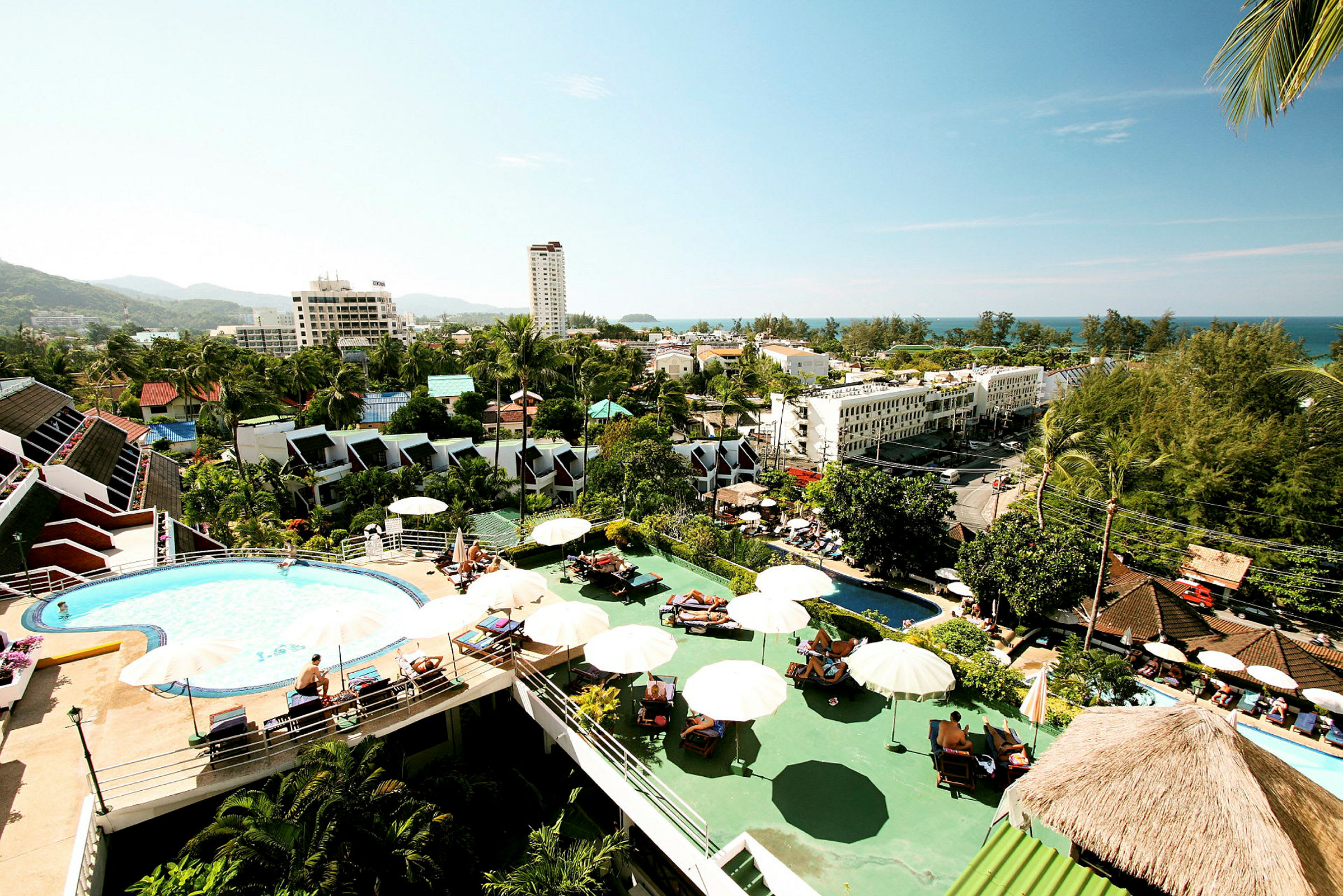Udsigt over hotelområde med pool, parasoller og bygninger i tropisk miljø. (AI-genereret tekst)