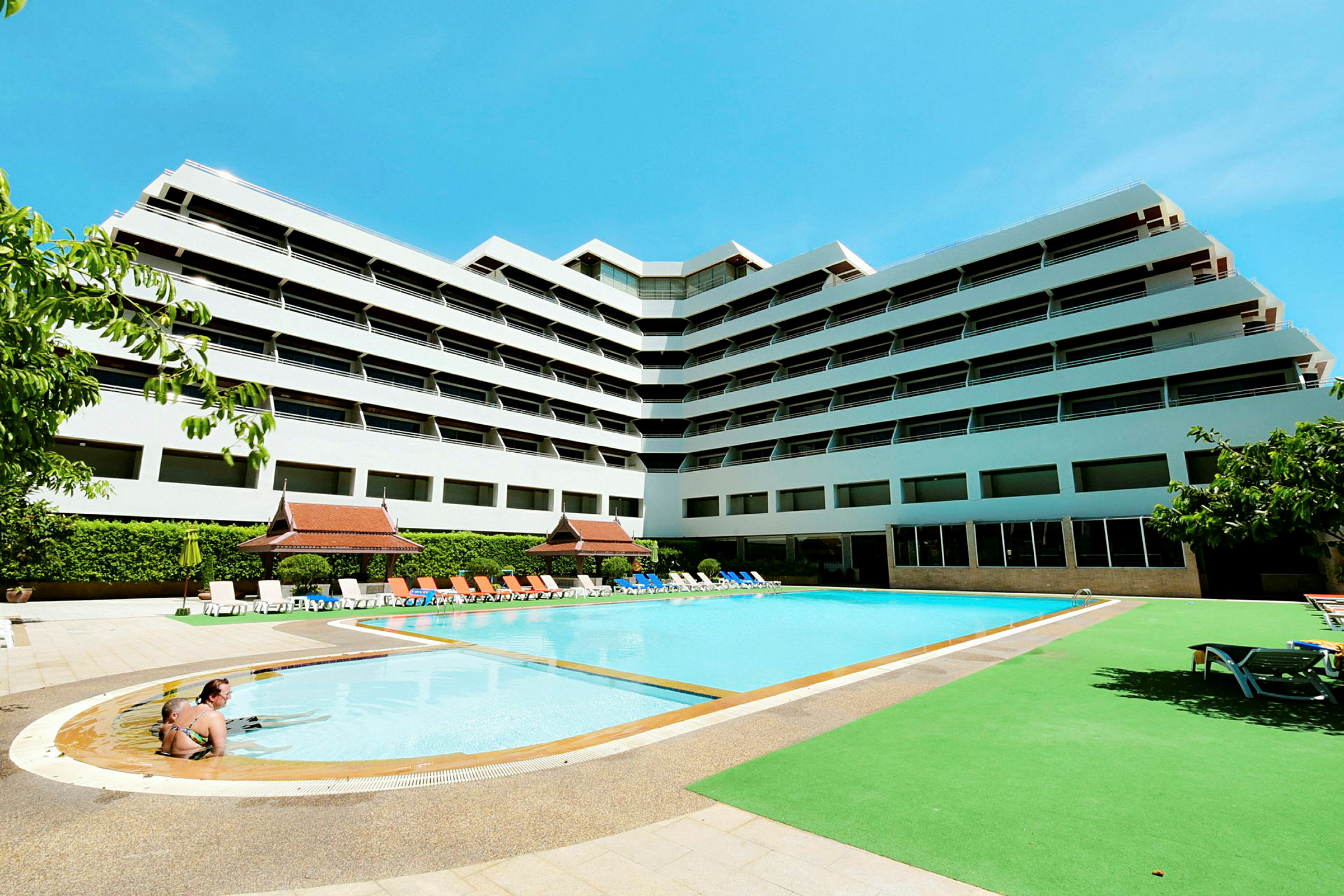 Moderne hotelbygning med pool og liggestole udenfor. (AI-genereret tekst)
