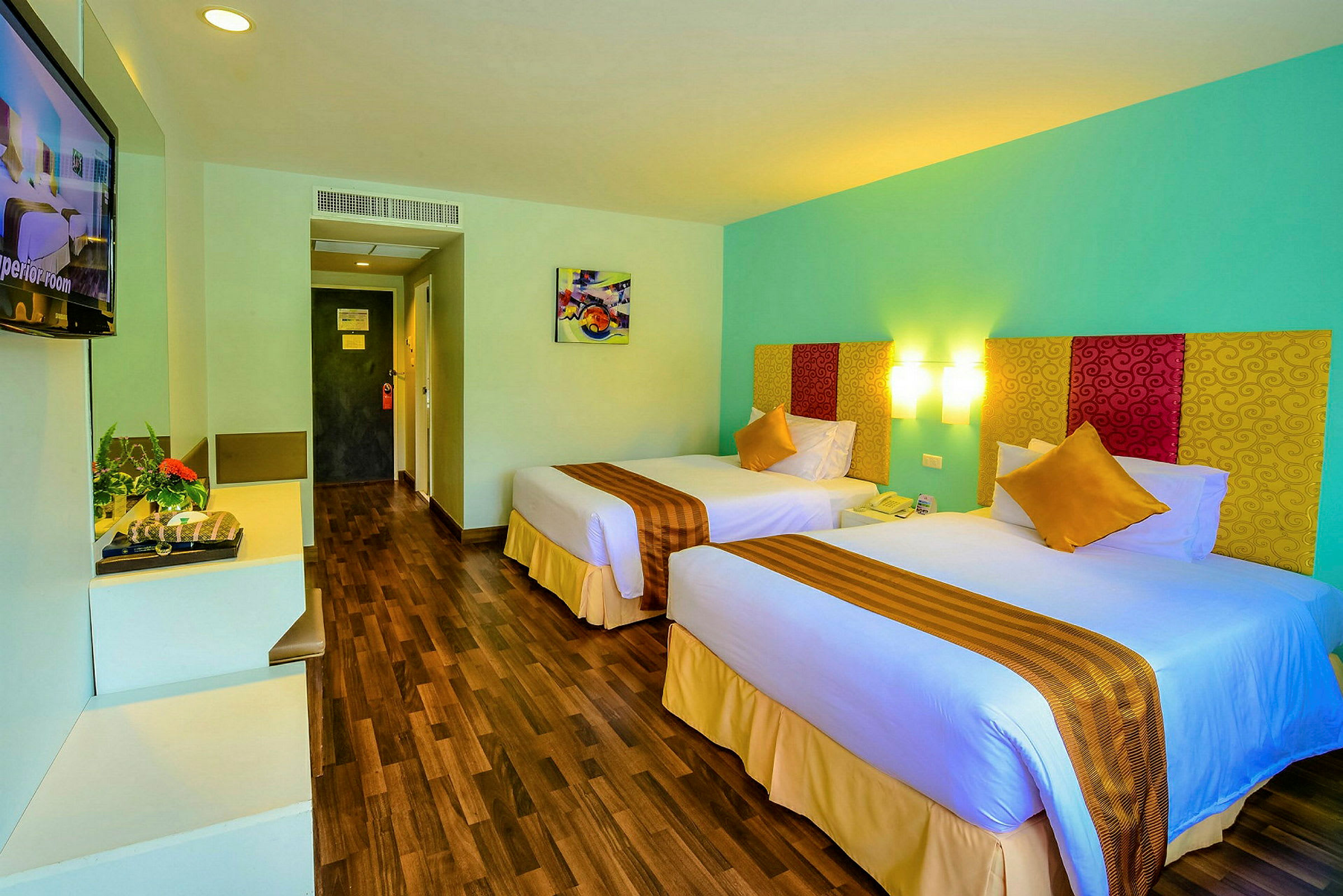 Hotelværelse med to enkeltsenge, farverige sengetæpper og vægkunst. (AI-genereret tekst)