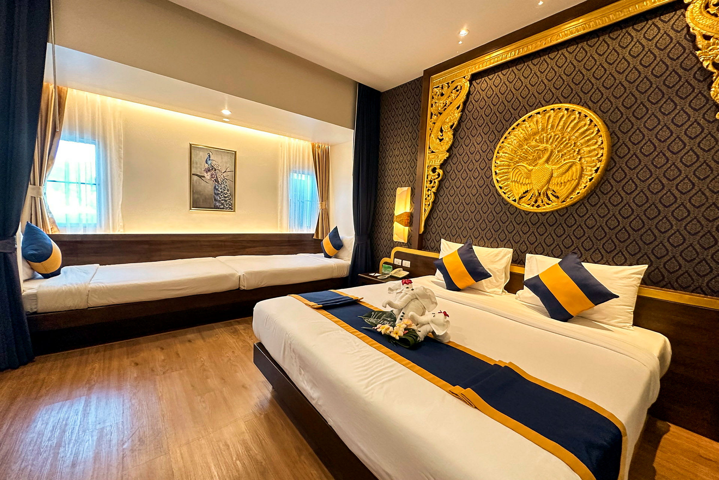 Hotelværelse med dobbeltseng og enkeltseng, dekoreret med blå og gule detaljer samt elegante guldfarvede ornamenter på væggen. (AI-genereret tekst)