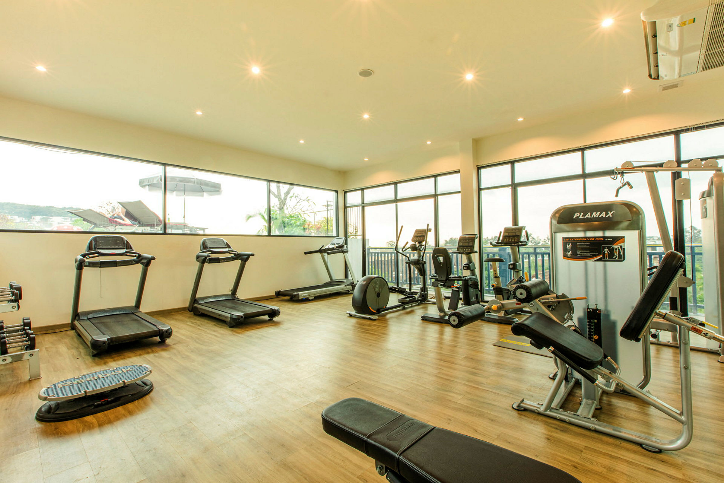 Et moderne fitnesscenter udstyret med løbebånd, motionscykler og vægtmaskiner i et lyst rum med store vinduer. (AI-genereret tekst)