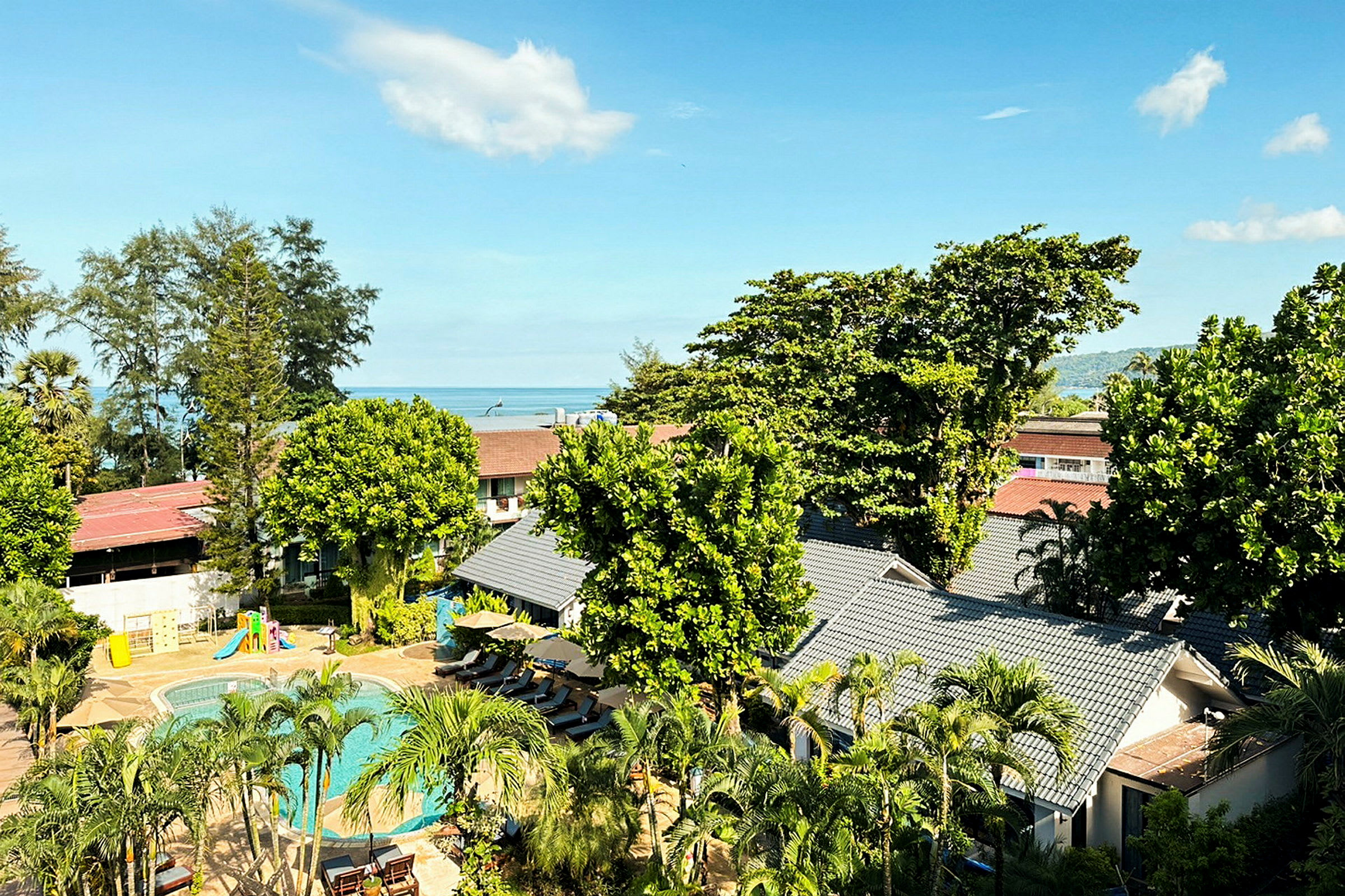 Udsigt over hotelområde med pool og frodighed, i baggrunden ses havet. (AI-genereret tekst)