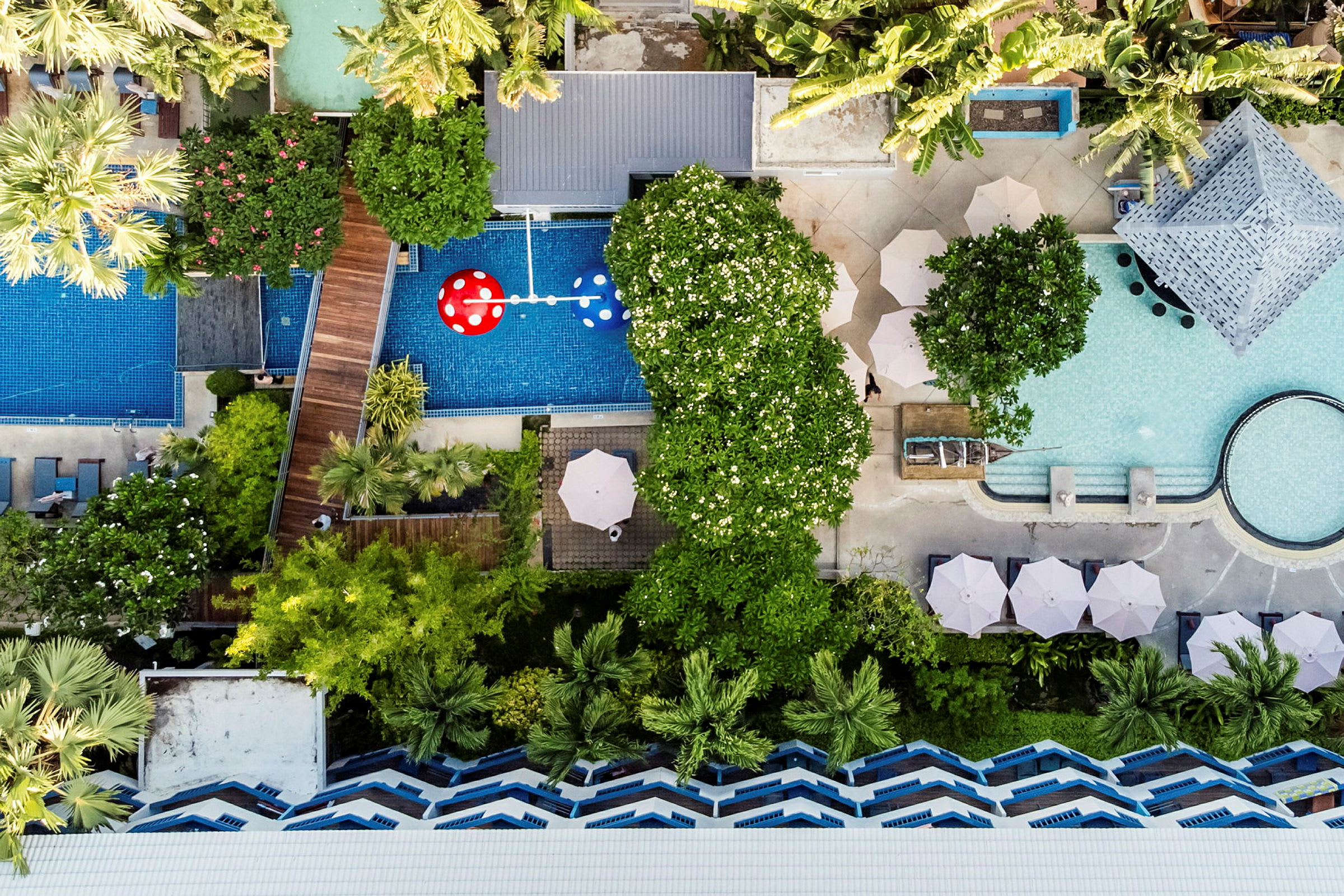 Luftfoto af et hotelområde med pooler, grønt og parasoller. (AI-genereret tekst)