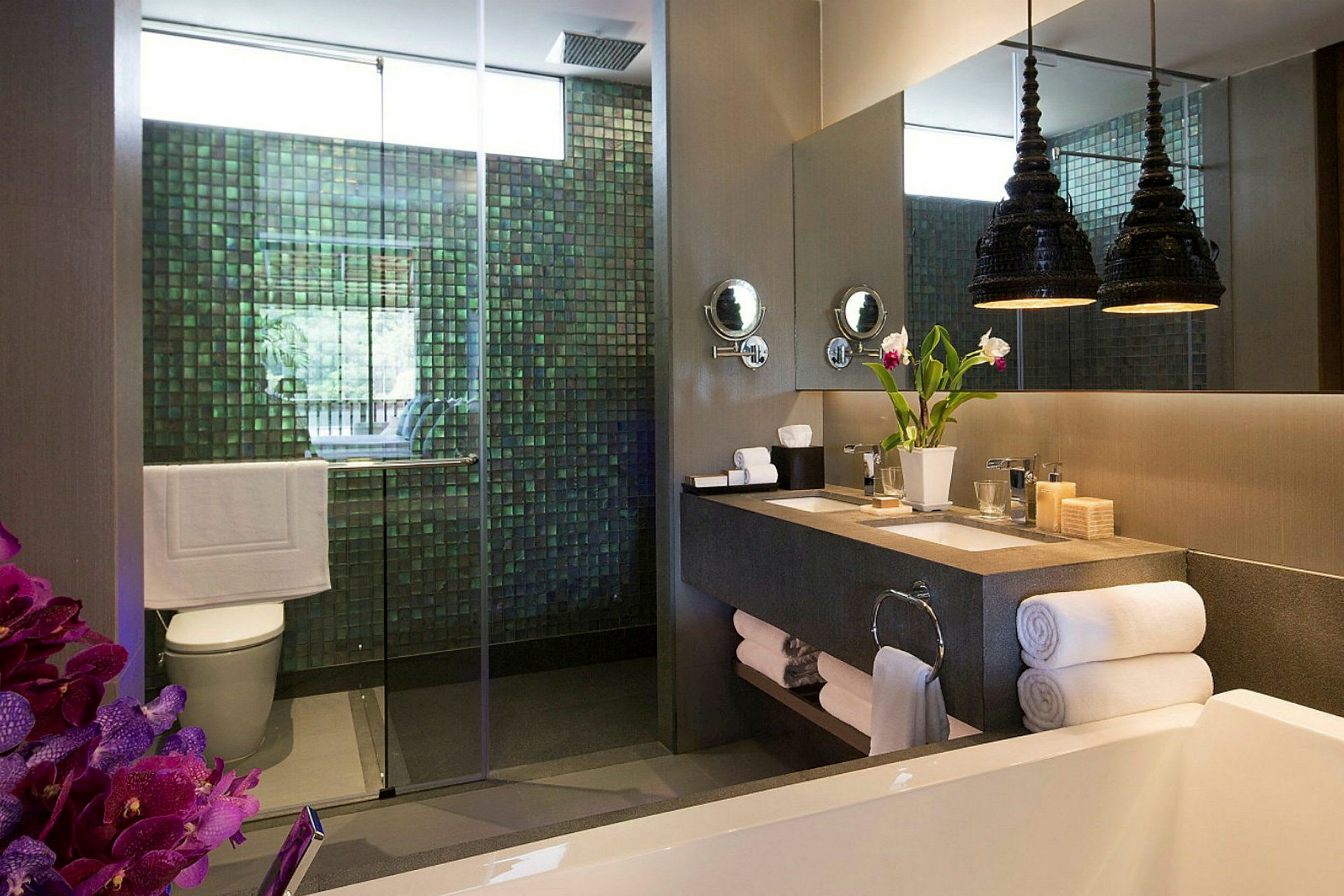 Et moderne badeværelse med en bruser med glasdør, en dobbeltvask med spejle ovenover, en dekorativ vase med blomster og håndklæder pænt stablet. (AI-genereret tekst)