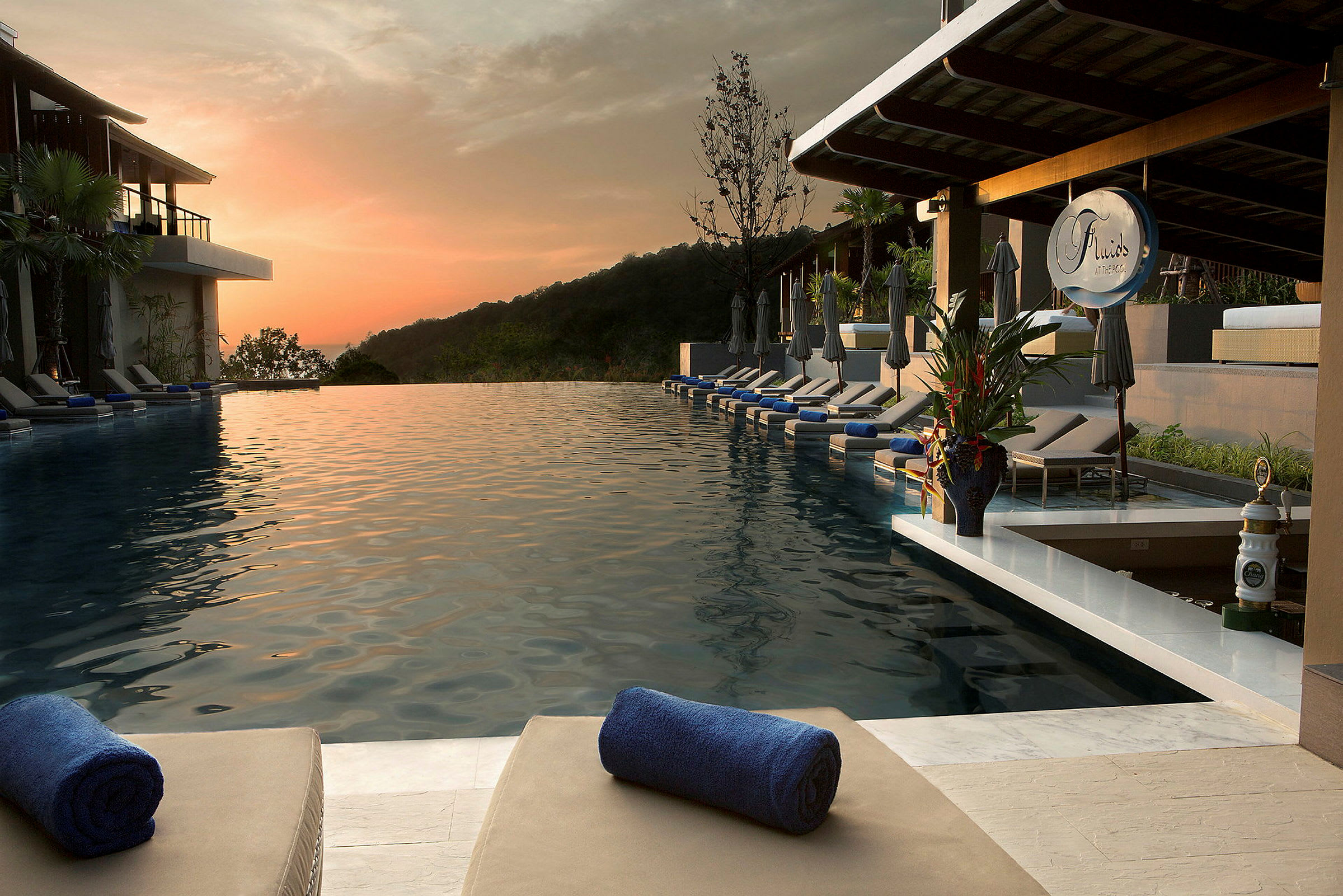 En infinitypool med solsenge og håndklæder på en ferieresort ved solnedgang. (AI-genereret tekst)