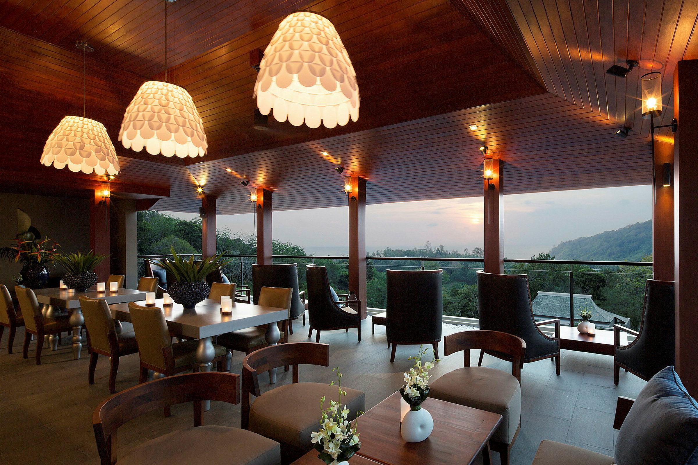 En moderne restaurant eller lounge med elegant indretning, store vinduer og udsigt over en skov og bakker i baggrunden. (AI-genereret tekst)