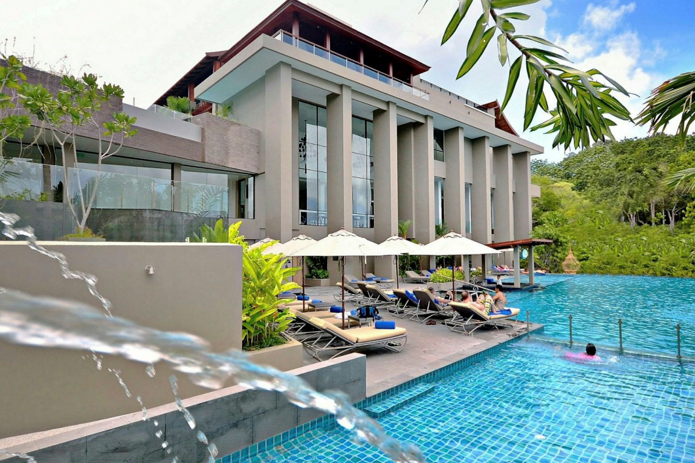 Billede af en hotelbygning ved en swimmingpool med liggestole og parasoller. (AI-genereret tekst)