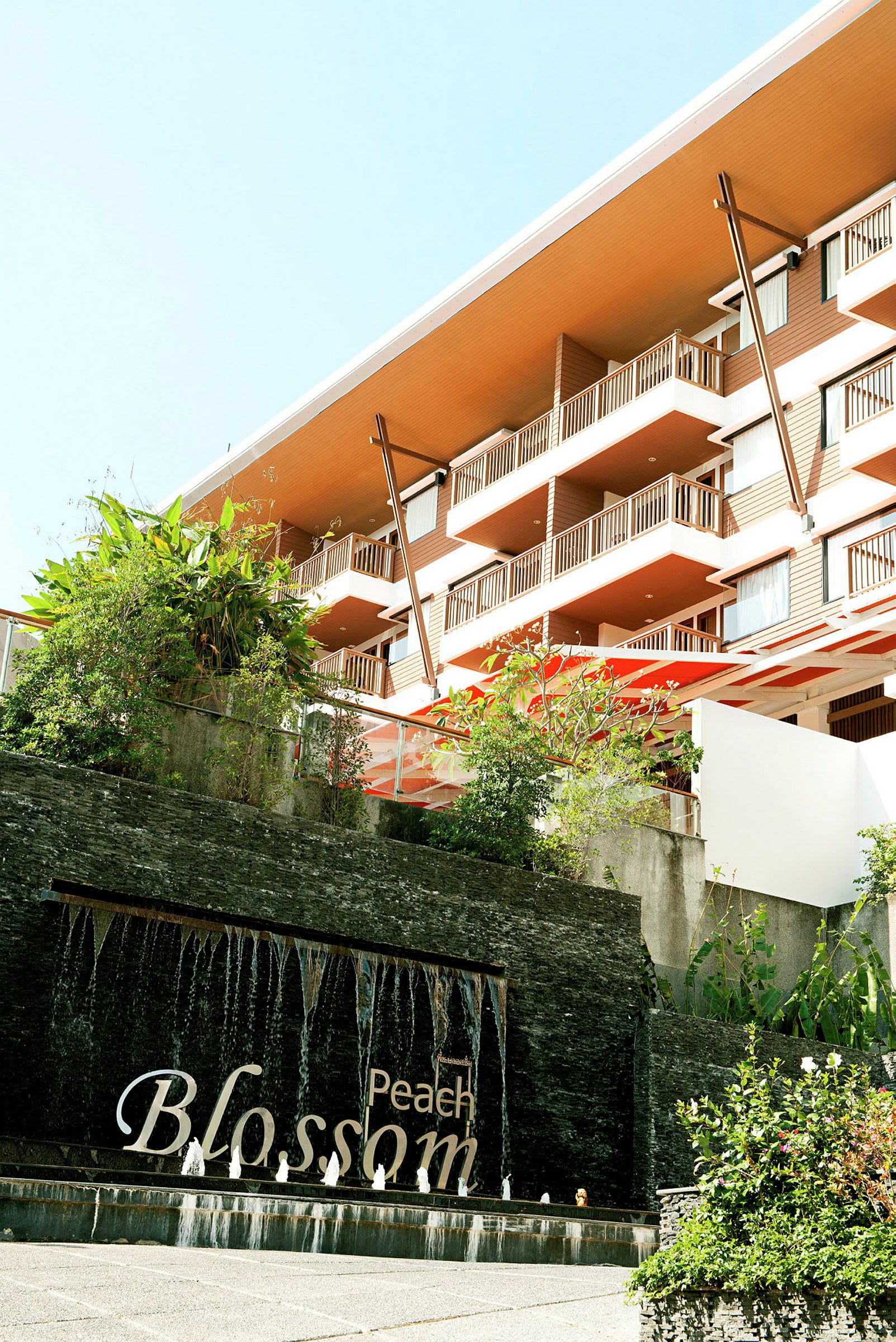 Et hotel med moderne altaner, grønne områder og en springvand med teksten "Peach Blossom". (AI-genereret tekst)