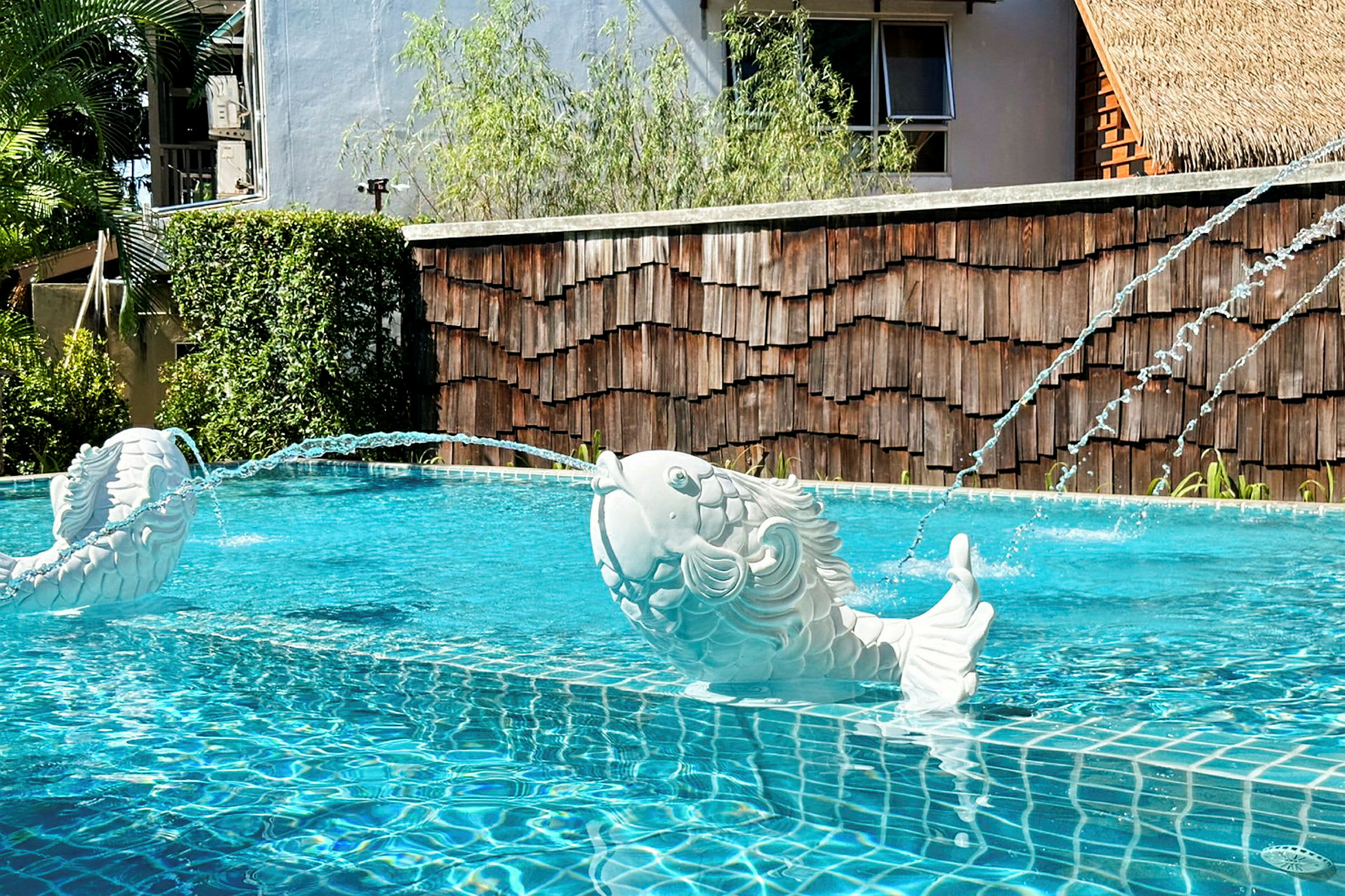Hvide skulpturer af fisk, der sprøjter vand i en pool. (AI-genereret tekst)