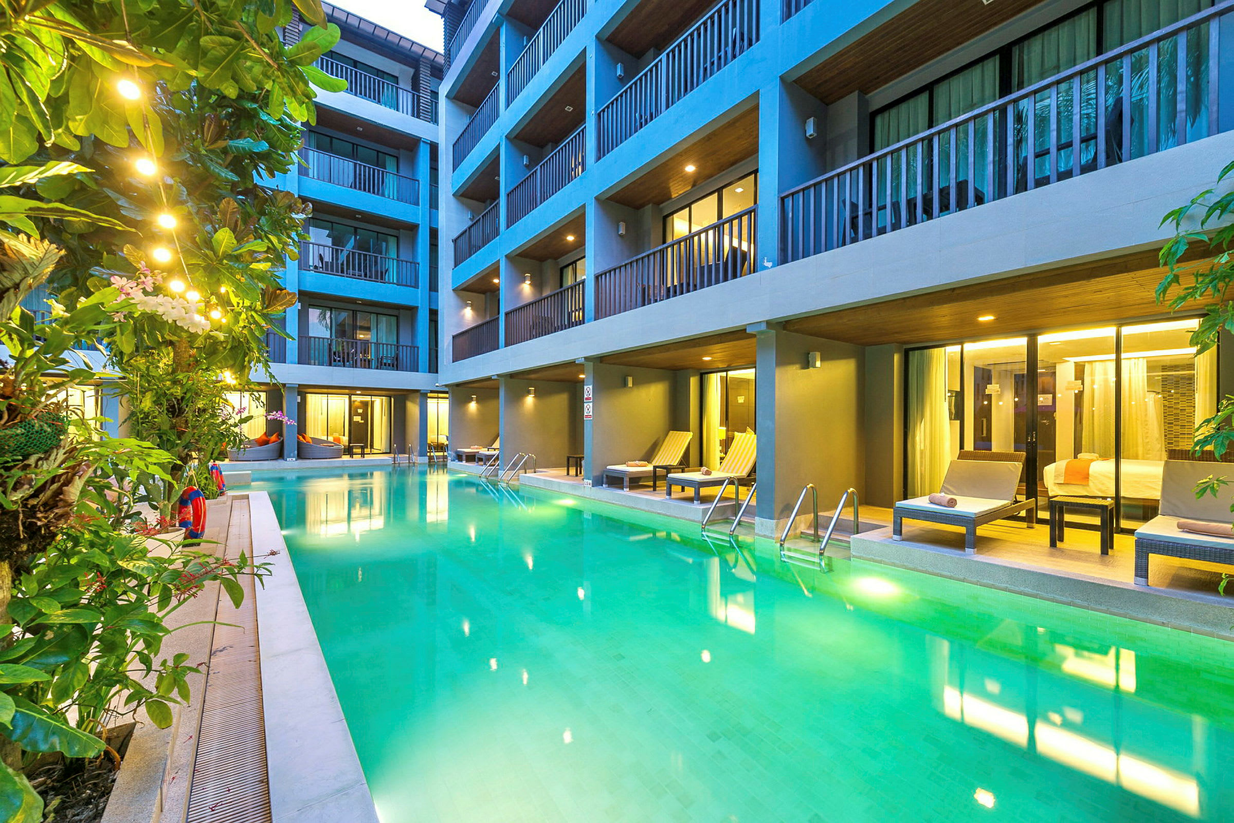 Pool med liggestole og omkringliggende planter foran hotelværelser. (AI-genereret tekst)