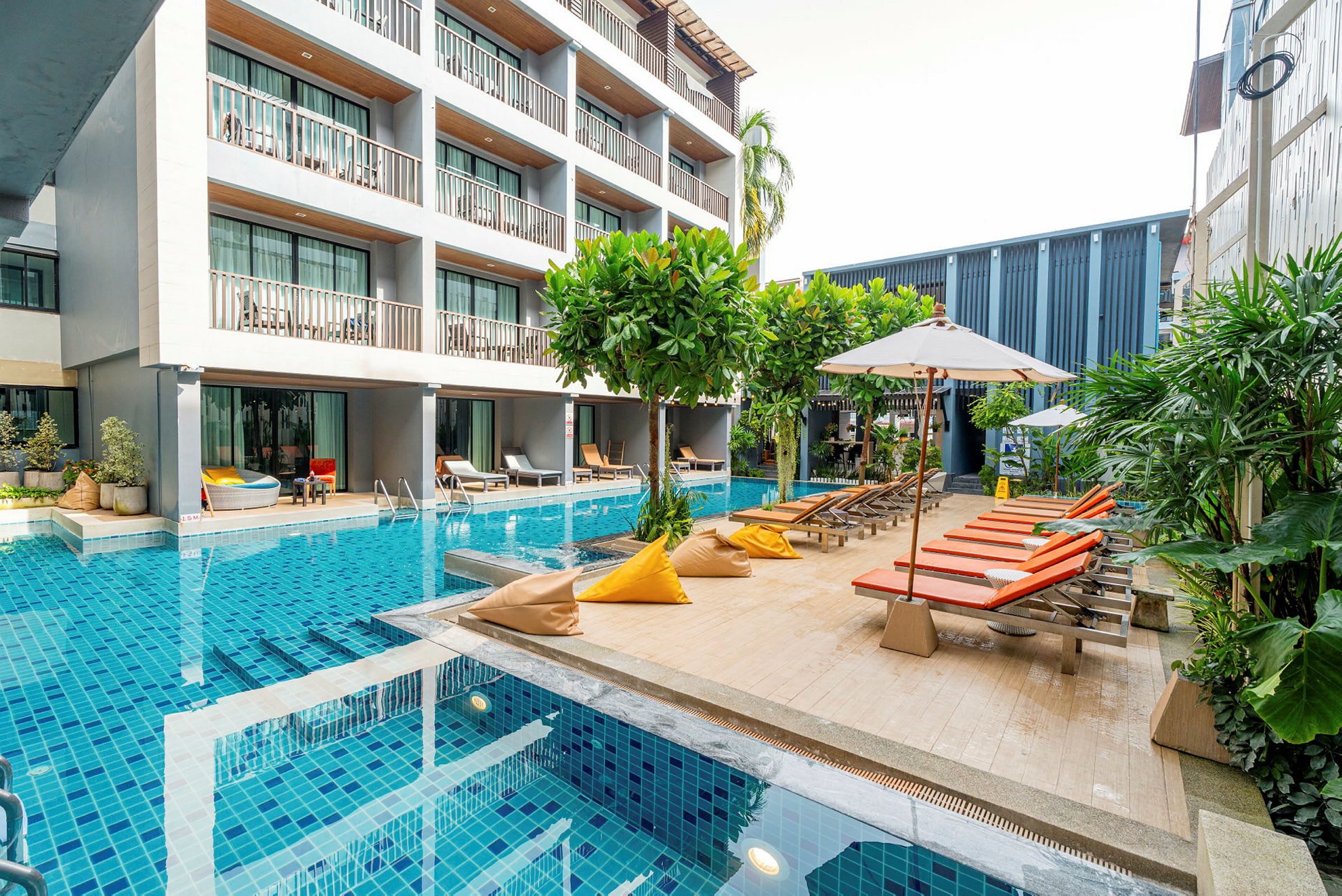 En moderne hotelbygning ved siden af en pool med liggestole og parasoller. (AI-genereret tekst)