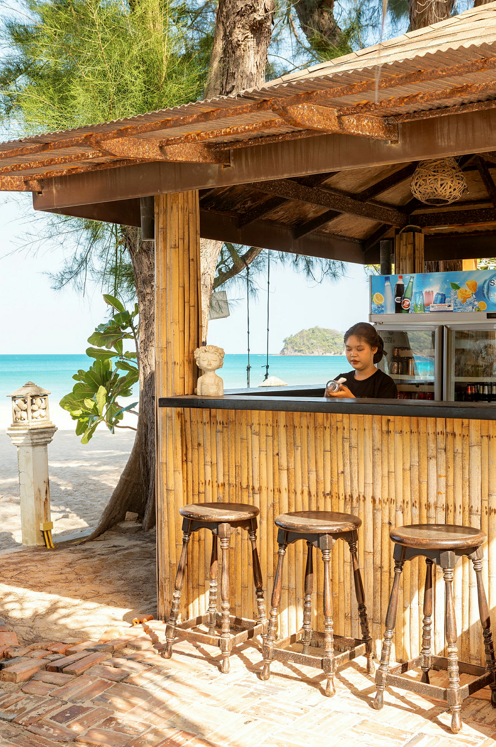En bar med bambusvægge, træskamler og strand i baggrunden. (AI-genereret tekst)