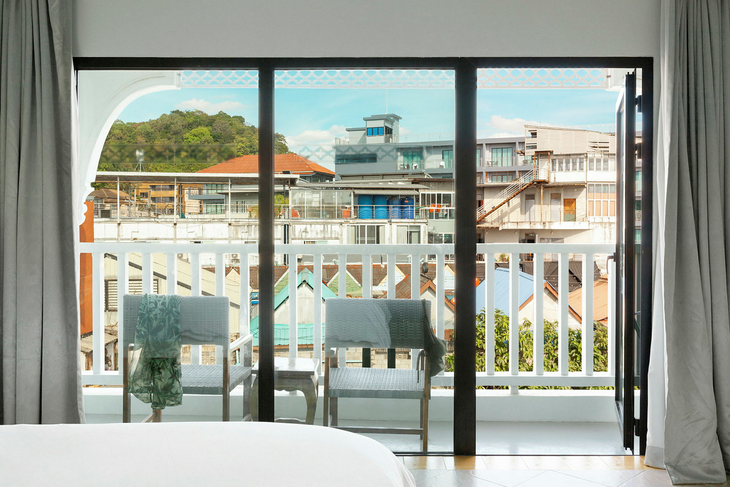 Udsigt gennem en stor glasrude, der åbner ud mod en balkon med udsigt over bymiljøet. (AI-genereret tekst)