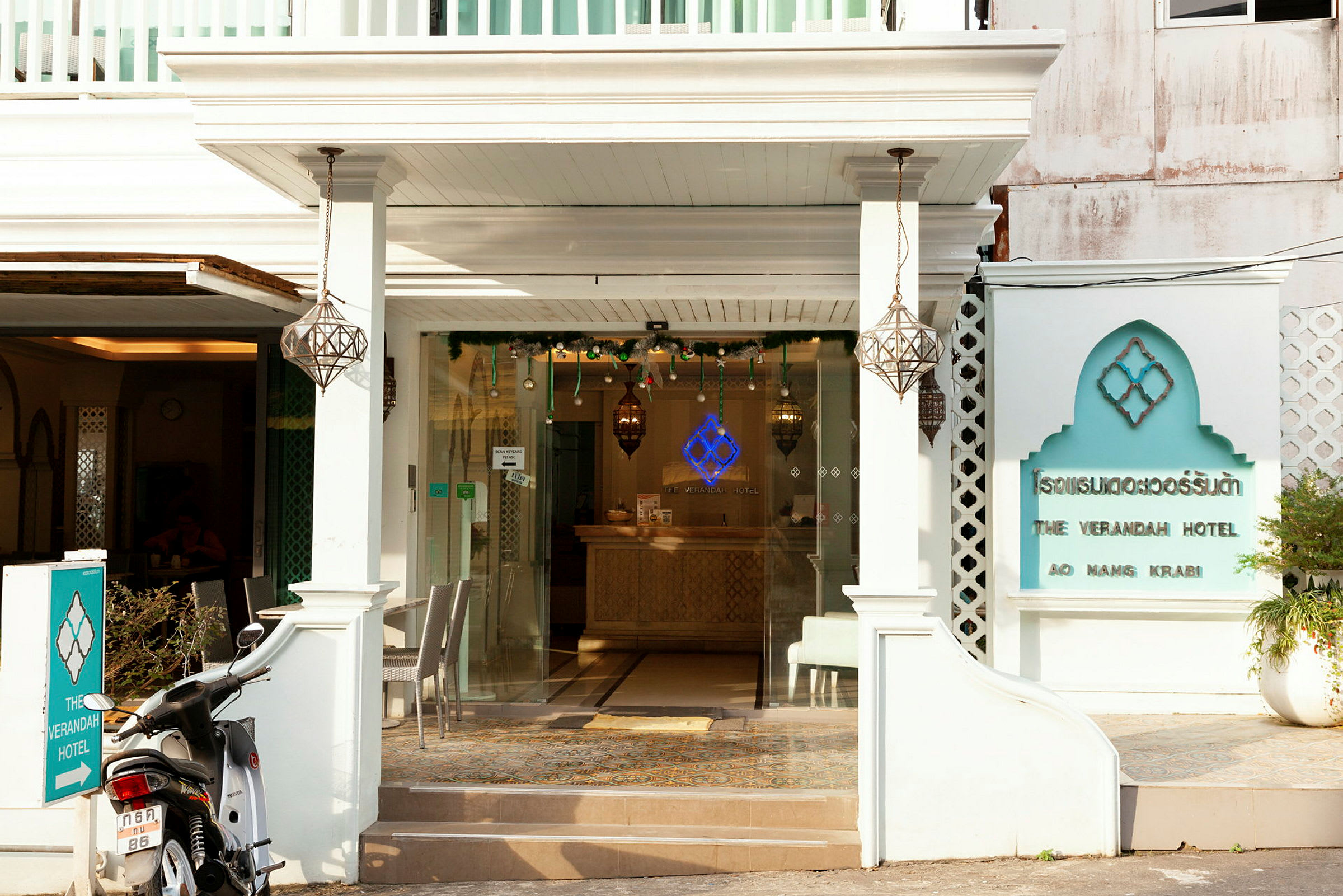 Forsiden af The Verandah Hotel med en motorcykel parkeret foran indgangen. (AI-genereret tekst)
