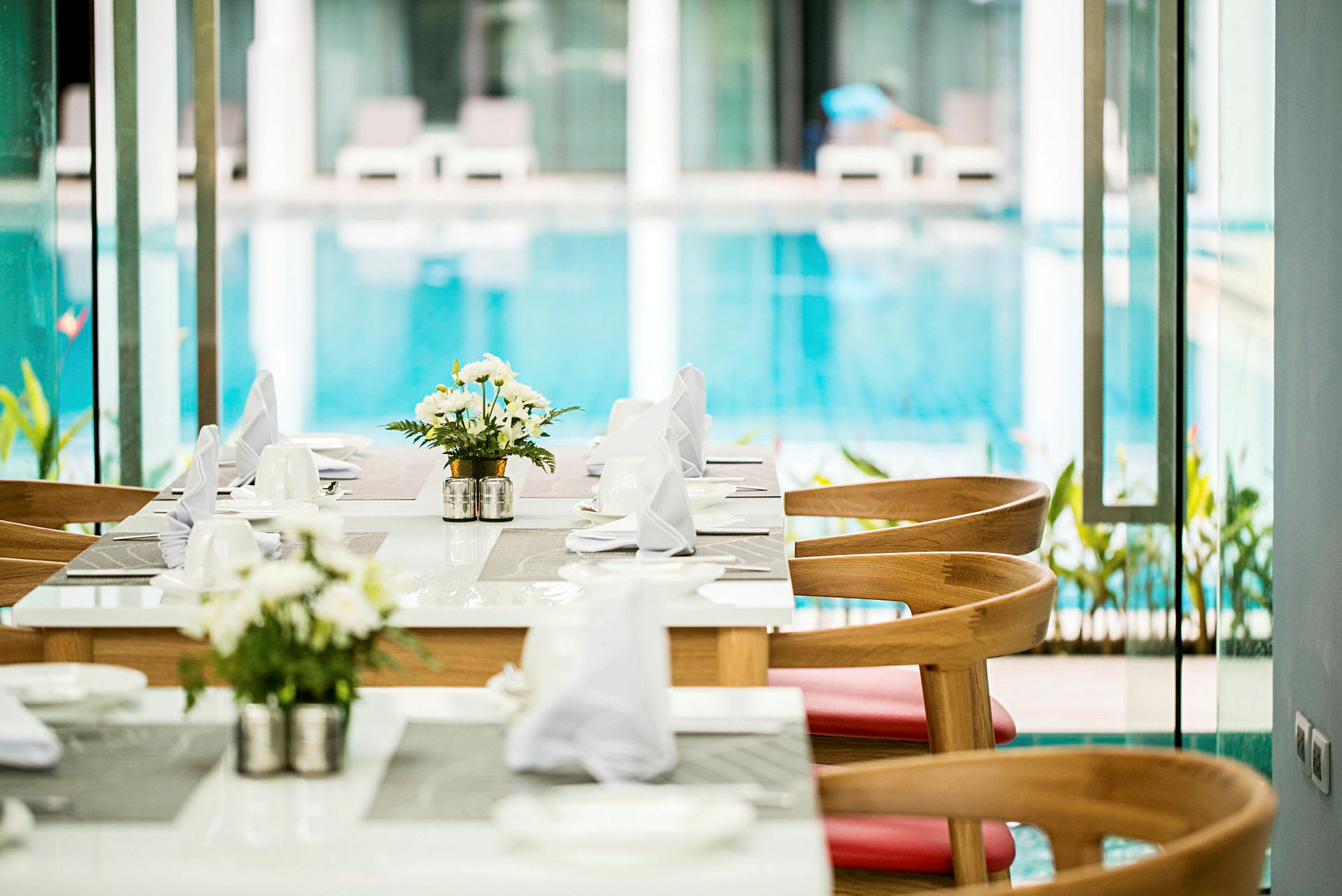 Et spisebord med duge og blomster ved siden af en pool. (AI-genereret tekst)