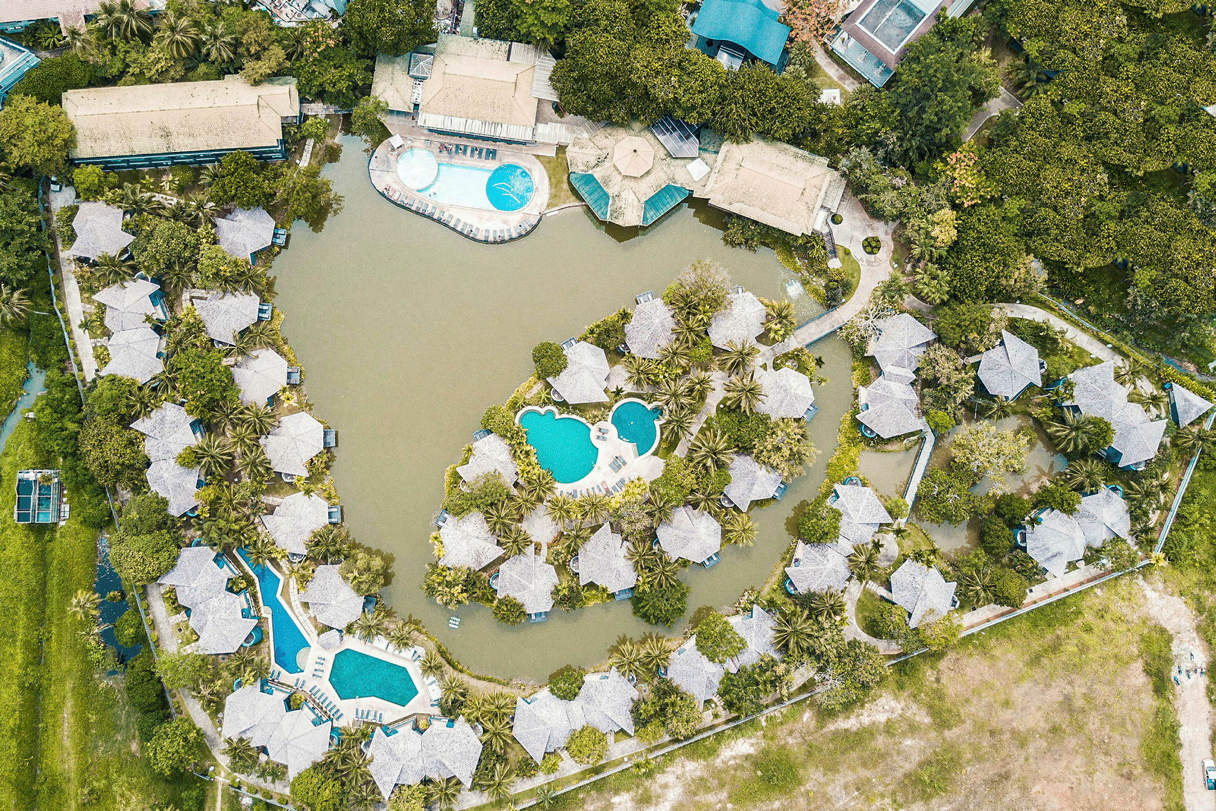 Fugleperspektiv af et ferieanlæg med bungalower, swimmingpools og grønne områder. (AI-genereret tekst)