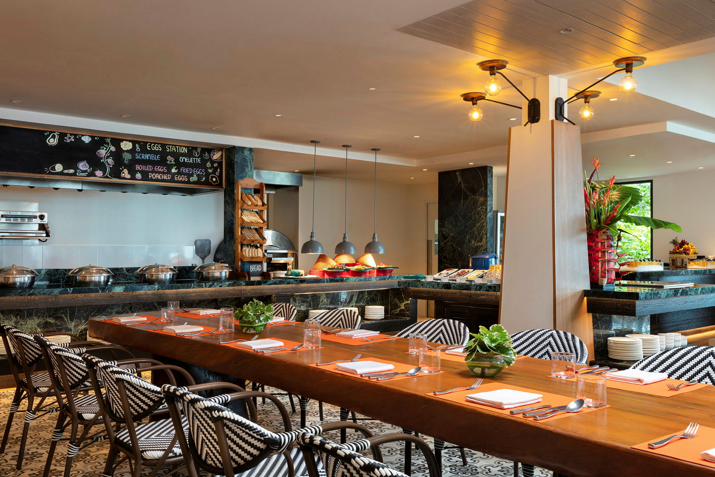 Interiør af en restaurant med et langt spisebord, stole med mønstrede sæder og en morgenmadsbuffet med mad og dekorationer. (AI-genereret tekst)
