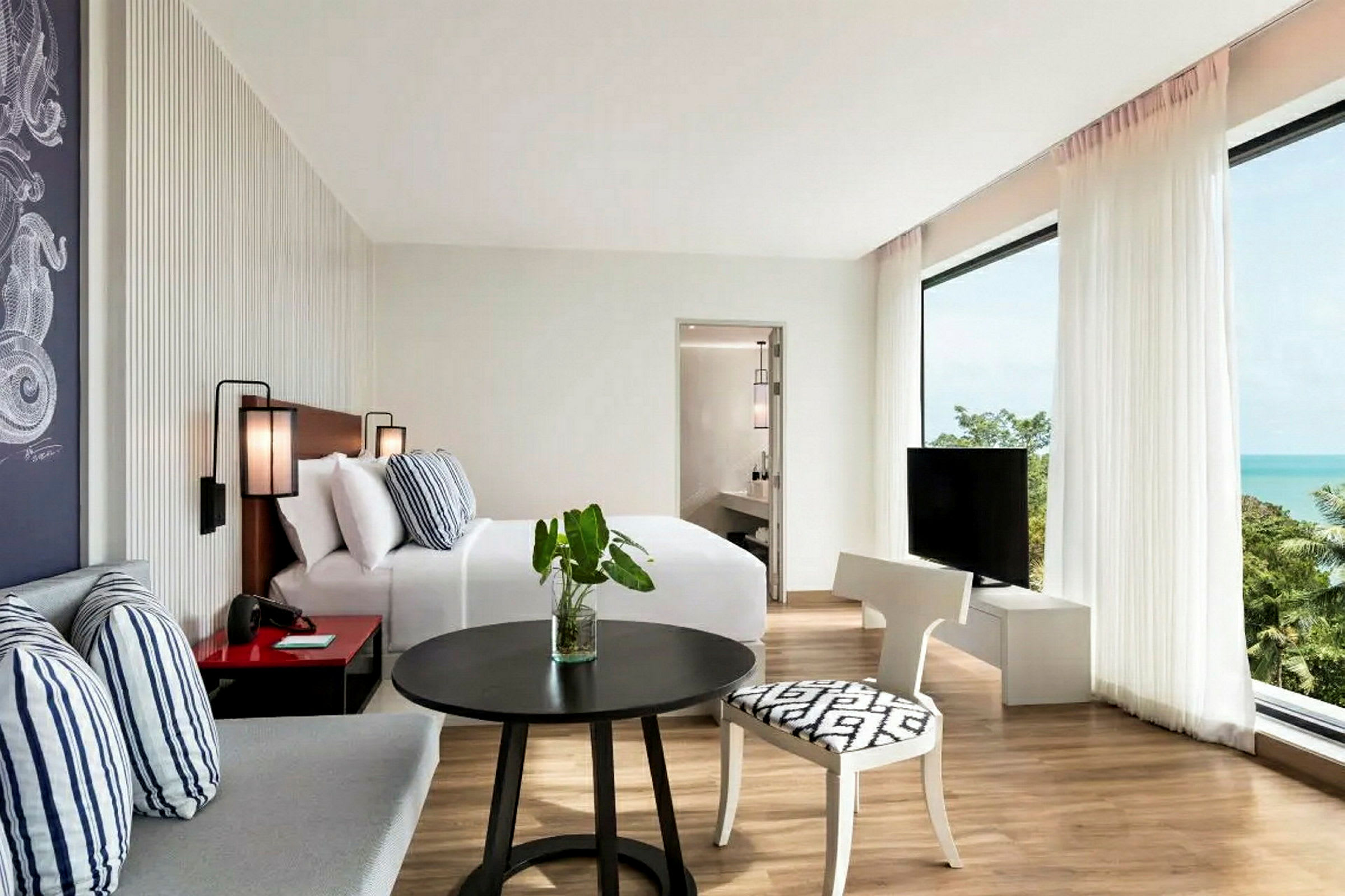 Et lyst hotelværelse med seng, siddeområde, tv og udsigt over havet. (AI-genereret tekst)