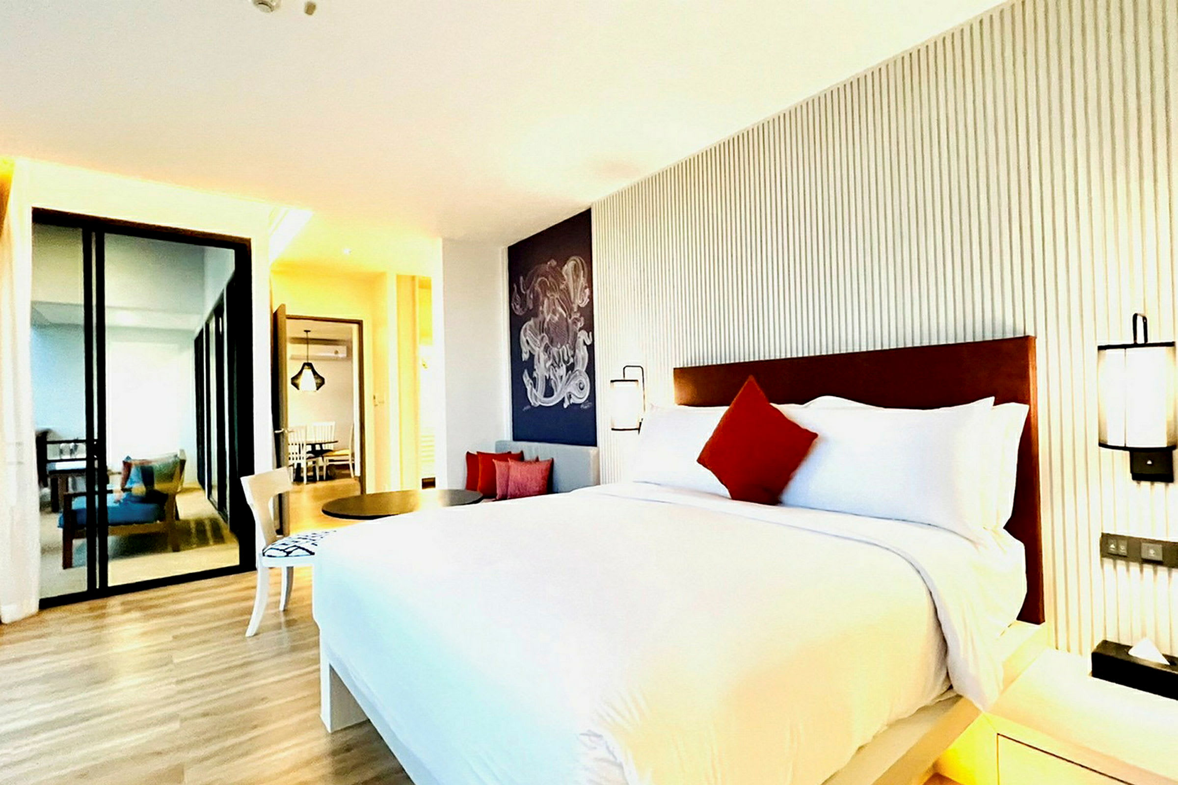 Et moderne hotelværelse med en stor seng, hvide og røde puder, minimalistisk indretning og trægulv. (AI-genereret tekst)