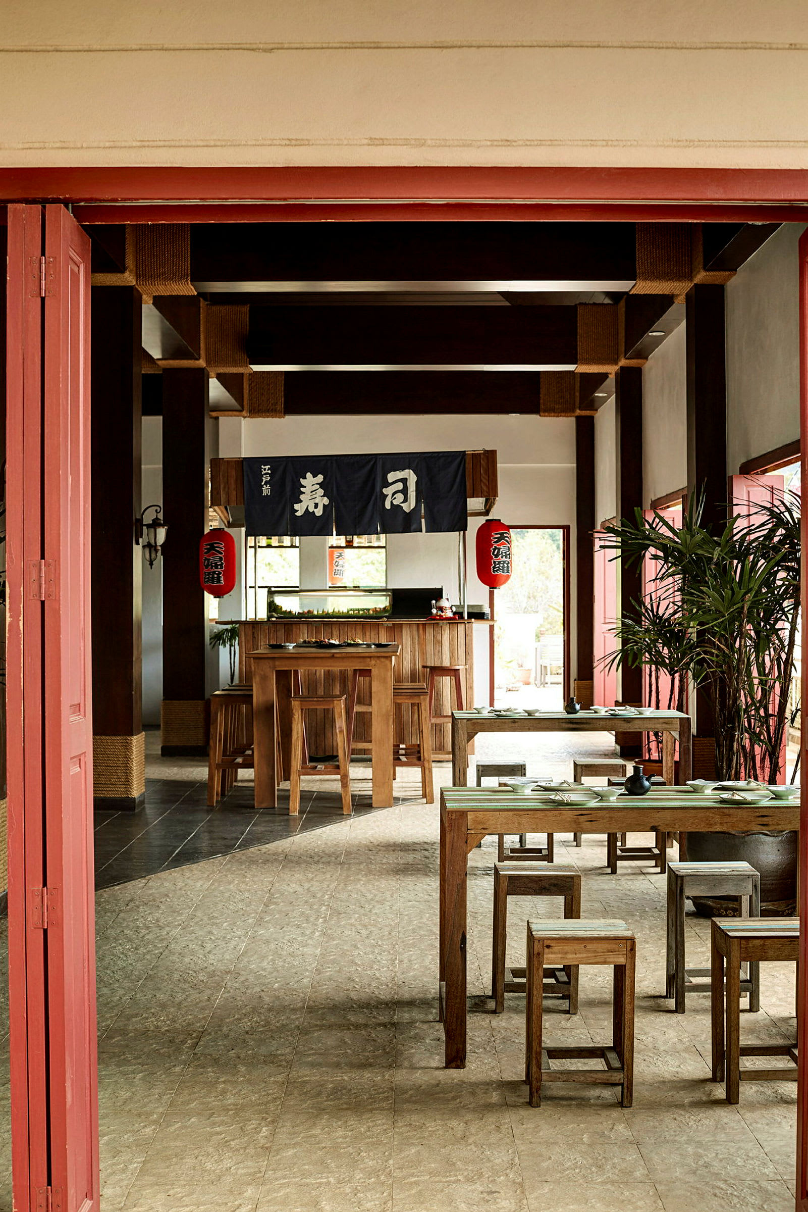 Et rum indrett som en japansk restaurant med træborde og stole, dekoreret med japanske lanterner og tekstil med japanske tegn. (AI-genereret tekst)