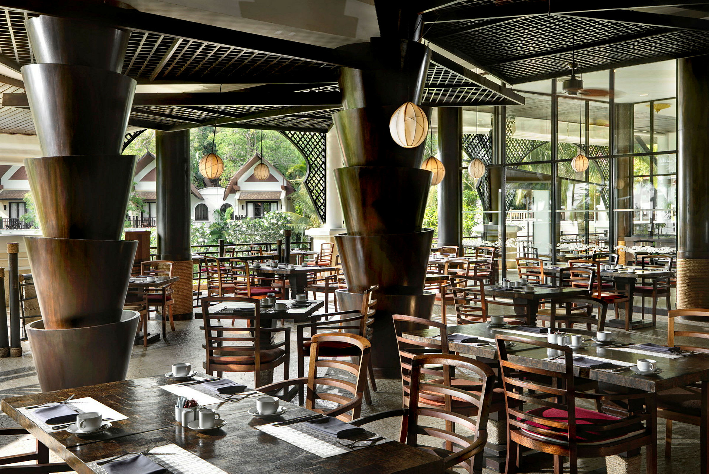 En moderne restaurant med elegante træborde og stole, omgivet af grønne områder og store vinduer. (AI-genereret tekst)