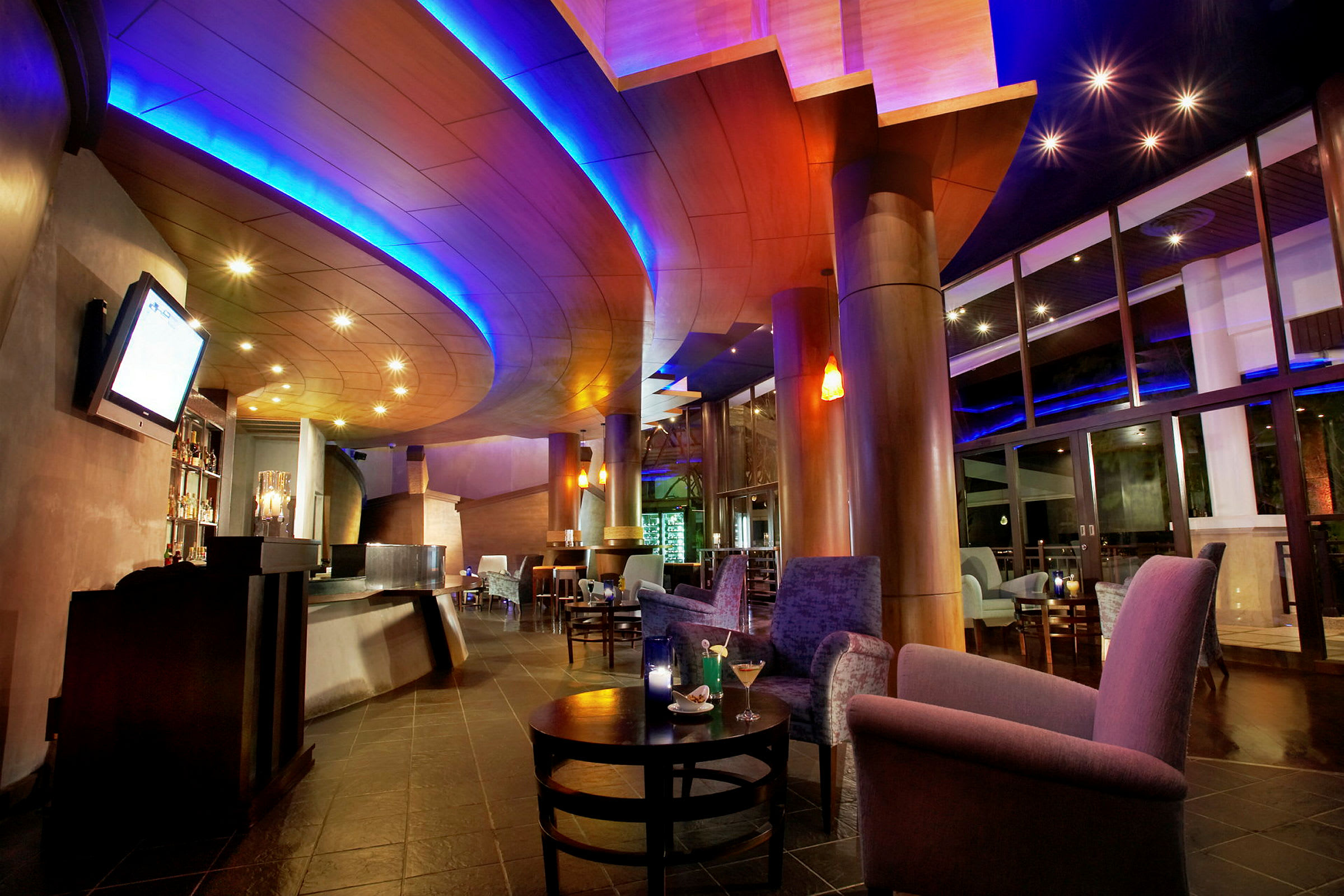 Et interiør af en moderne lounge eller bar med et buet loftsdesign, bløde lænestole og sofaer samt stilfuld belysning i rummet. (AI-genereret tekst)