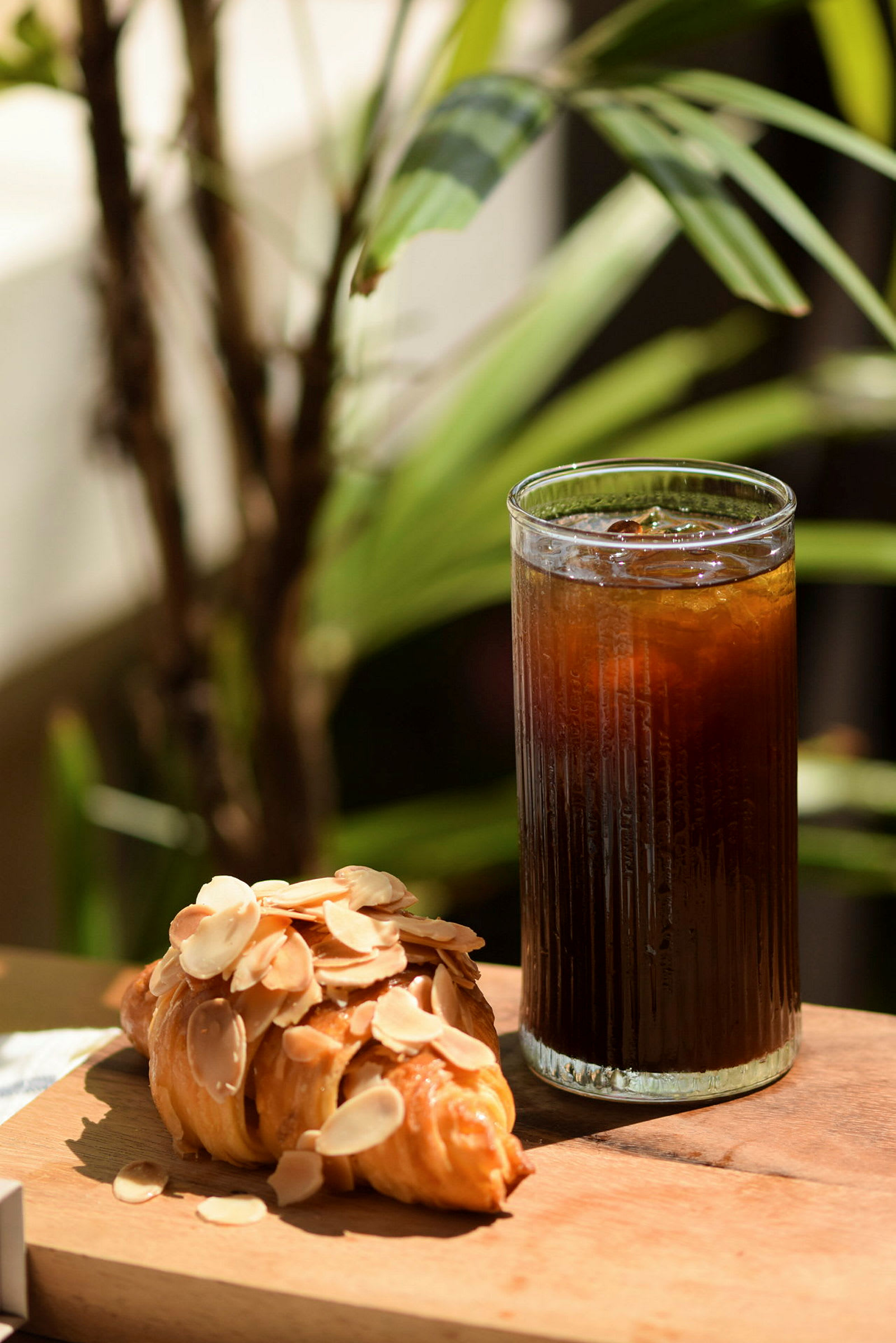 Et glas med kølig drik og en croissant dækket med mandelflager, placeret på et træbord. (AI-genereret tekst)