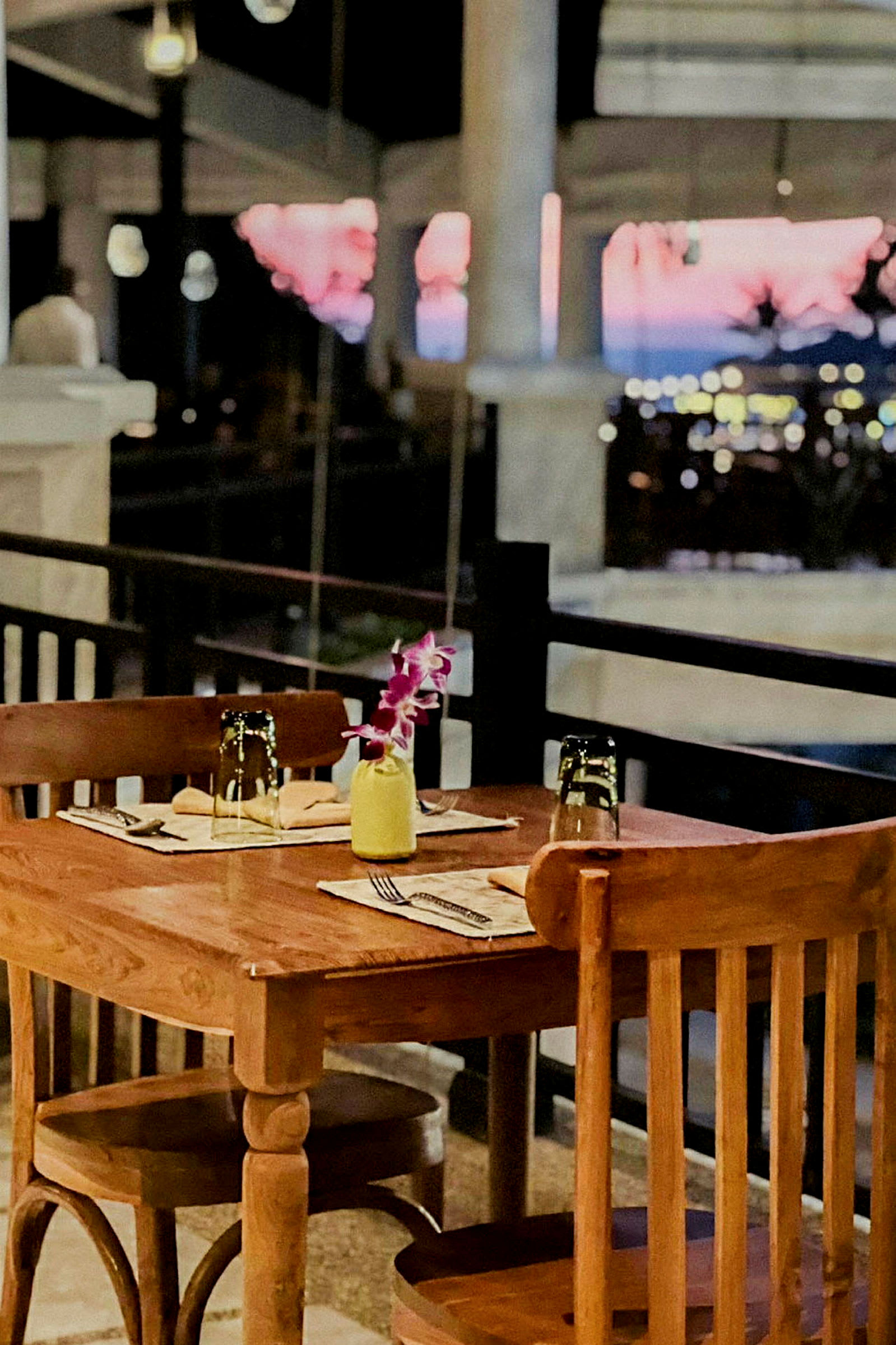 Et dækket træbord med to stole ved en restaurantterrasse og baggrund med sløret udsigt over aftenlandskab. (AI-genereret tekst)